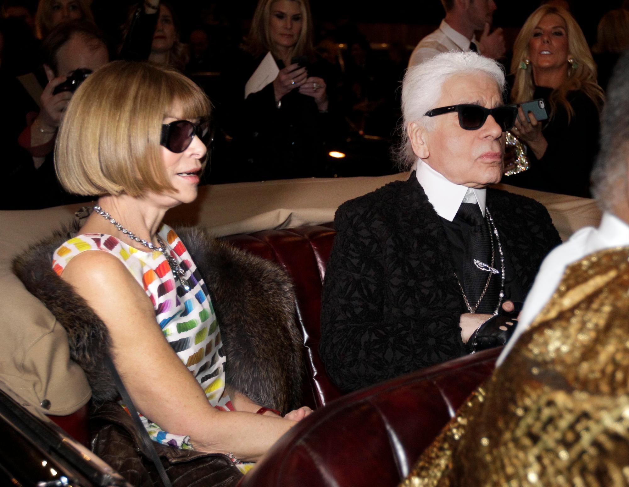  Anna Wintour, a la izquierda, la editora en jefe de la Vogue americana y el diseñador Karl Lagerfeld se sientan en un coche de época mientras esperan para ver una película corta de regreso de Coco Chanel a la moda después de cerrar su casa durante la segunda guerra mundial antes del inicio de los Metiers d’Art de Chanel Desfile de modas, en Dallas. 