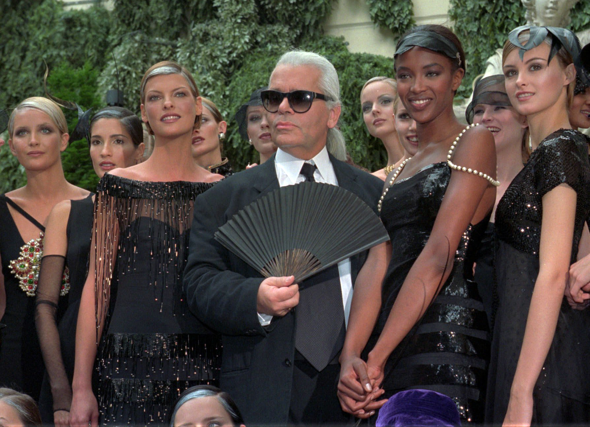 En la foto de archivo del 9 de julio de 1996 , Karl Lagerfeld está rodeada por la modelo canadiense Linda Evangelista, a la izquierda, y la modelo británica Naomi Campbell, a la derecha, y otros modelos después de la presentación de su 1996-97 otoño-invierno de alta costura de la colección de moda para Chanel en París.