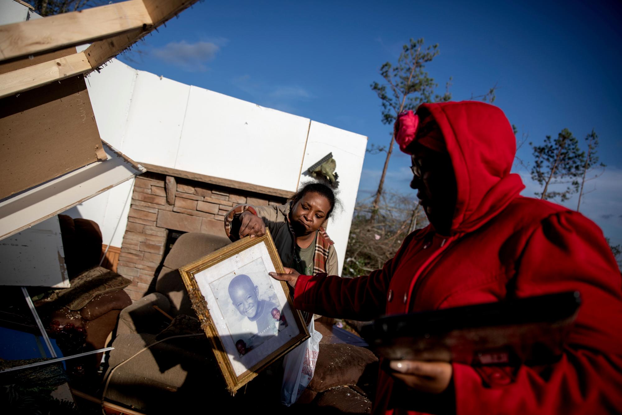 Shiraka Baker, a la izquierda, le pasa una foto de su hijo a su hija, Kiara Slater, mientras recupera artículos personales de su casa dañada,  donde sobrevivió a un tornado el día anterior en Beauregard, Alabama, el lunes 4 de marzo de 2019.