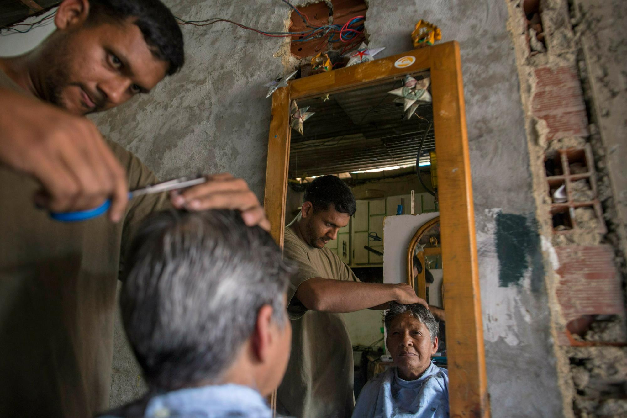 En esta foto del 14 de febrero de 2019, Jorge Flores practica sus habilidades de peluquería con su madre Rose Vega dentro de su casa, donde está tratando de establecer una peluquería en el barrio de Petare, en Caracas, Venezuela. 