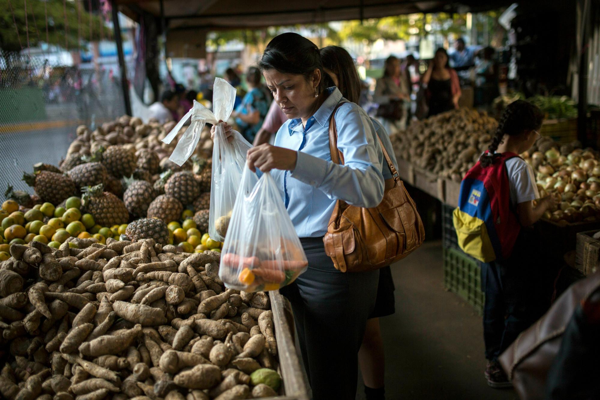En esta foto del 14 de febrero de 2019, Carmen Victoria Giménez, de 43 años, compra en un mercado de agricultores en el distrito de clase media de Los Dos Caminos, en Caracas, Venezuela. “Gano mucho más que el precio mínimo y sigo luchando”, dijo. “Ni siquiera puedo imaginar cómo sobreviven los más pobres entre los pobres”.