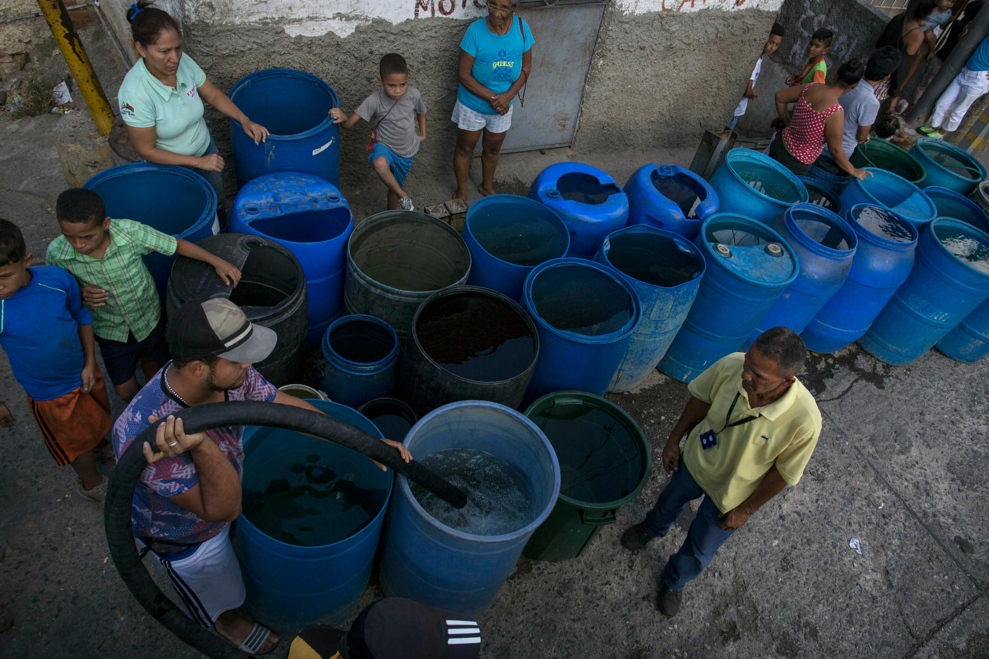 En esta foto del 14 de febrero de 2019, la gente espera mientras un trabajador llena los tanques de almacenamiento con agua potable en el barrio pobre de Petare, en Caracas, Venezuela. Notoriamente pobres, los residentes de los barrios pobres luchan a diario con agua corriente escasa y frecuentes apagones.