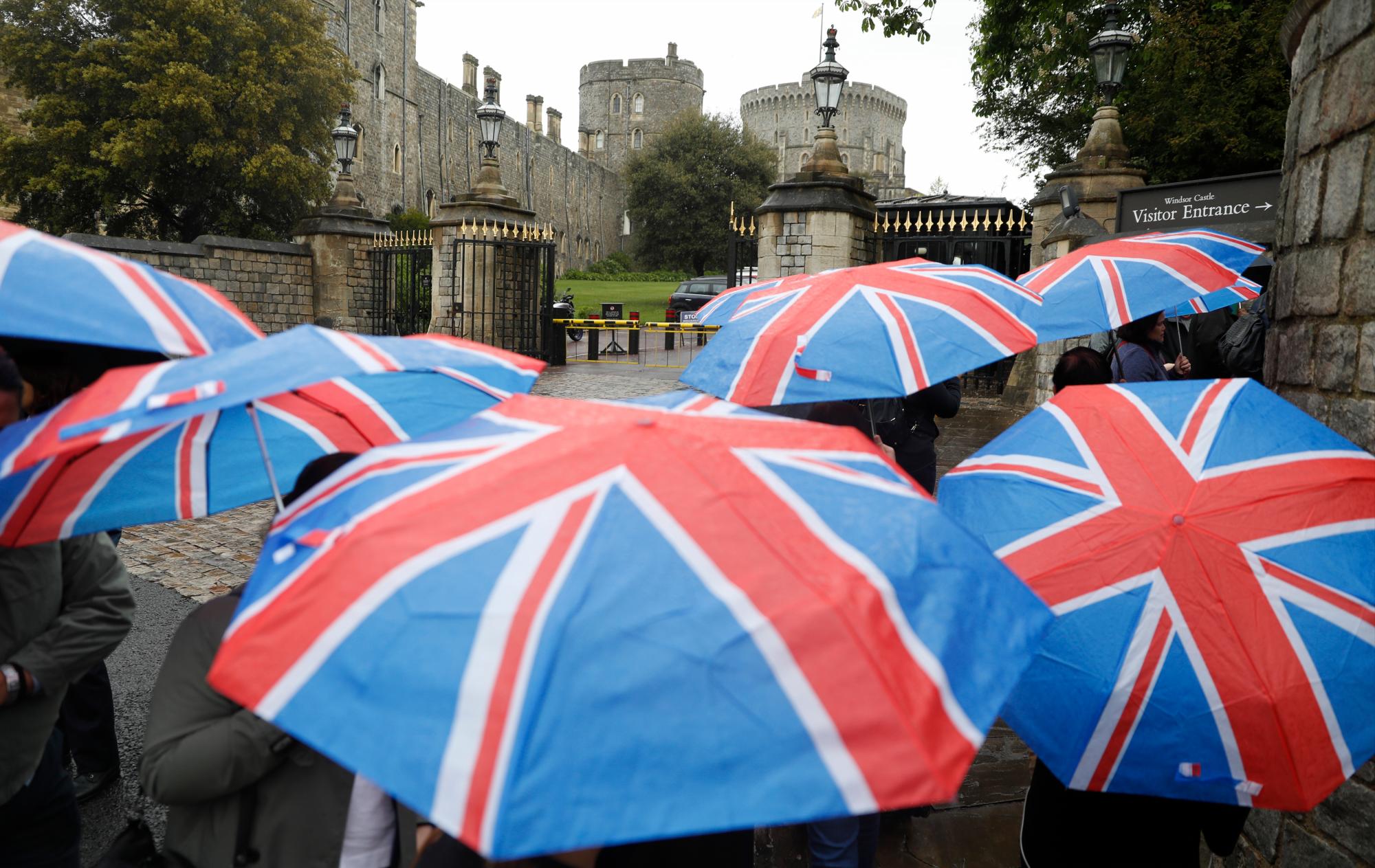 Los turistas con paraguas de la bandera de la Unión Británica caminan en la lluvia hacia la entrada al castillo de Windsor en Windsor, Inglaterra el miércoles 8 de mayo de 2019. Se espera que el príncipe Harry y Meghan, Duquesa de Sussex, presenten a su hijo recién nacido. 