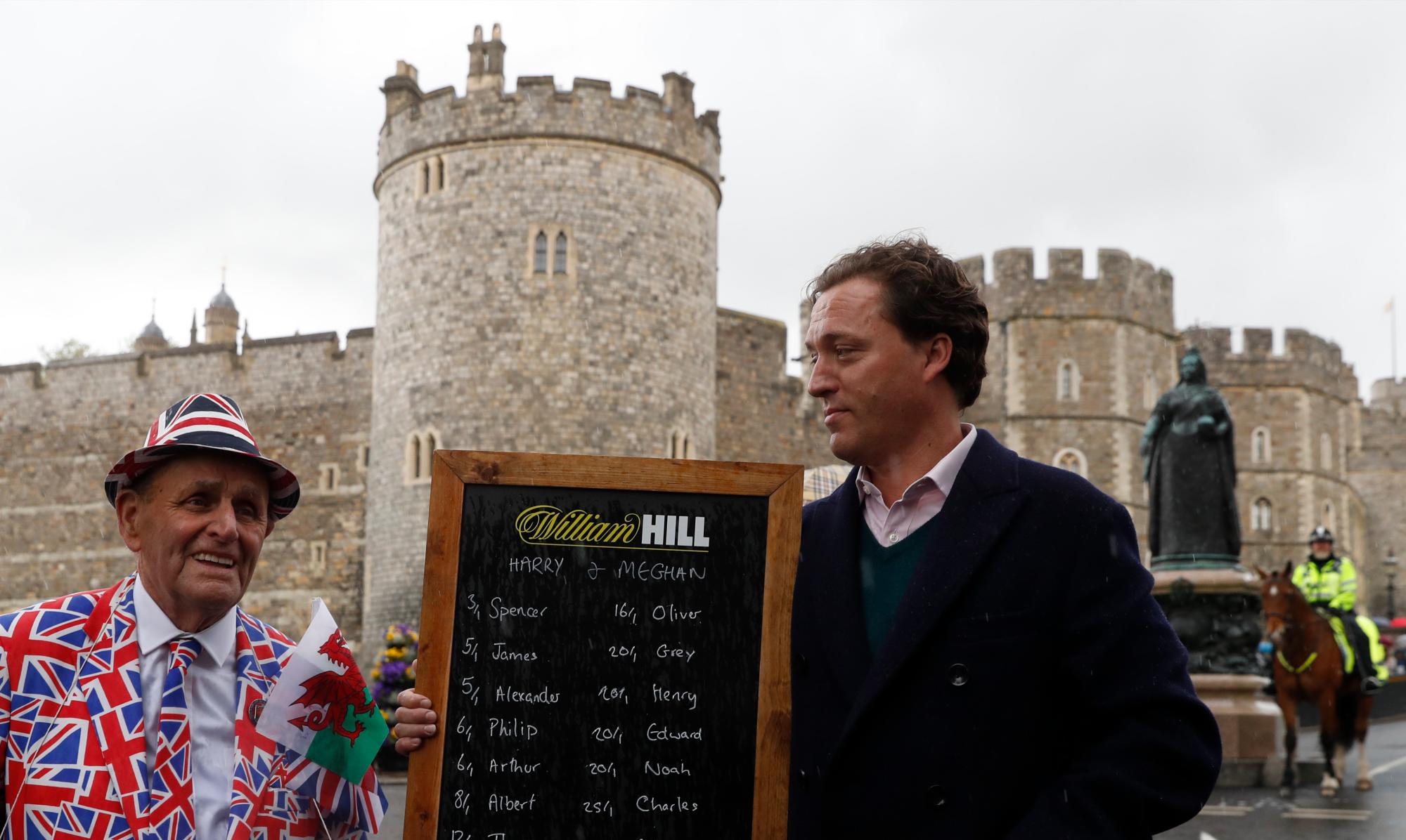 El fanático real Terry Hutt, a la izquierda, posa con Rupert Adams de la casa de apuestas británica William Hill mostrando una lista de las probabilidades en los nombres para el bebé hijo sin nombre del príncipe Harry y Meghan, Duquesa de Sussex afuera del castillo de Windsor.