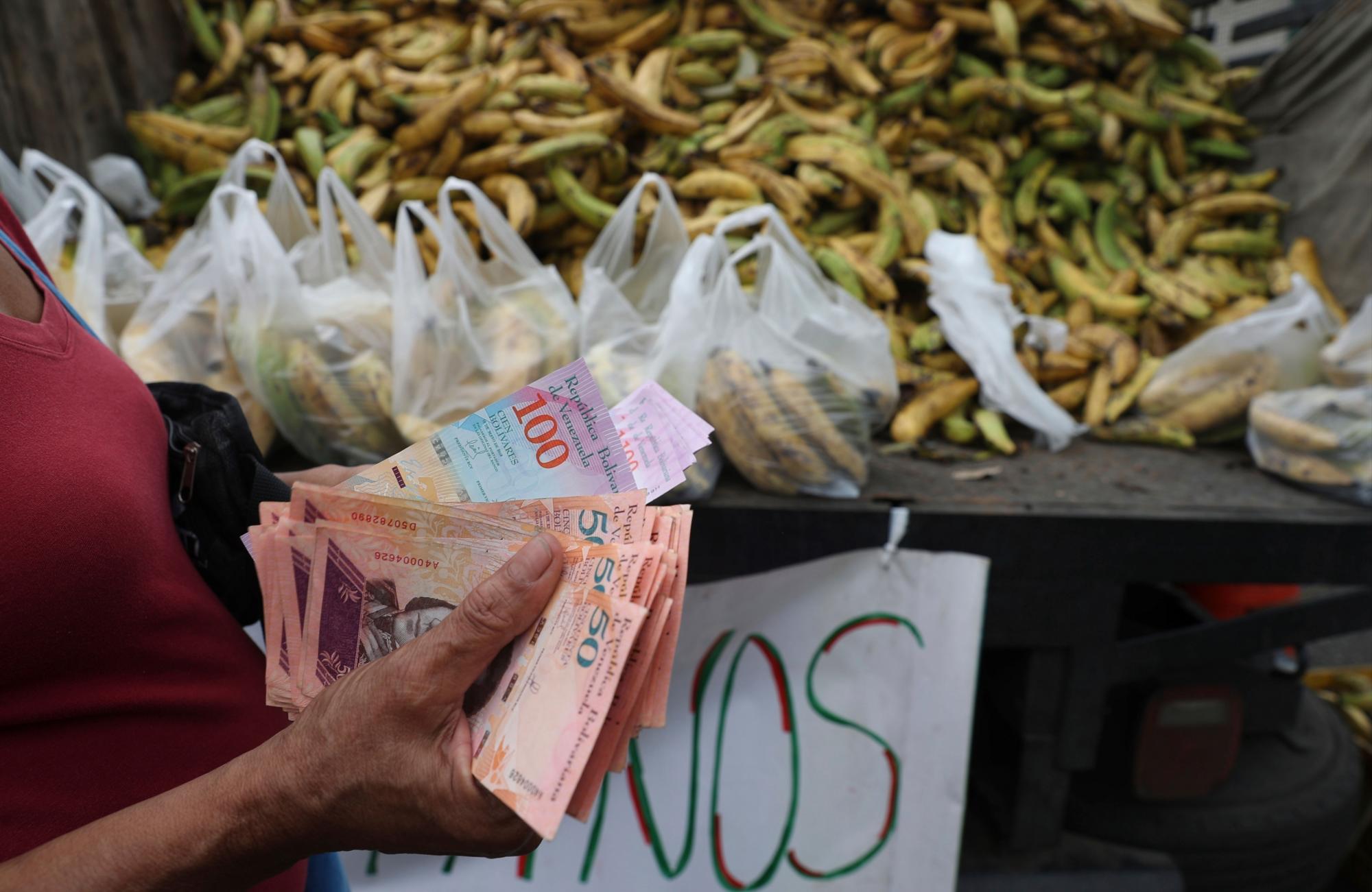 En esta foto del 8 de mayo de 2019, una mujer cuenta cinco mil bolívares, casi un dólar, para comprar una penca de plátanos en el área de Petare en Caracas, Venezuela.