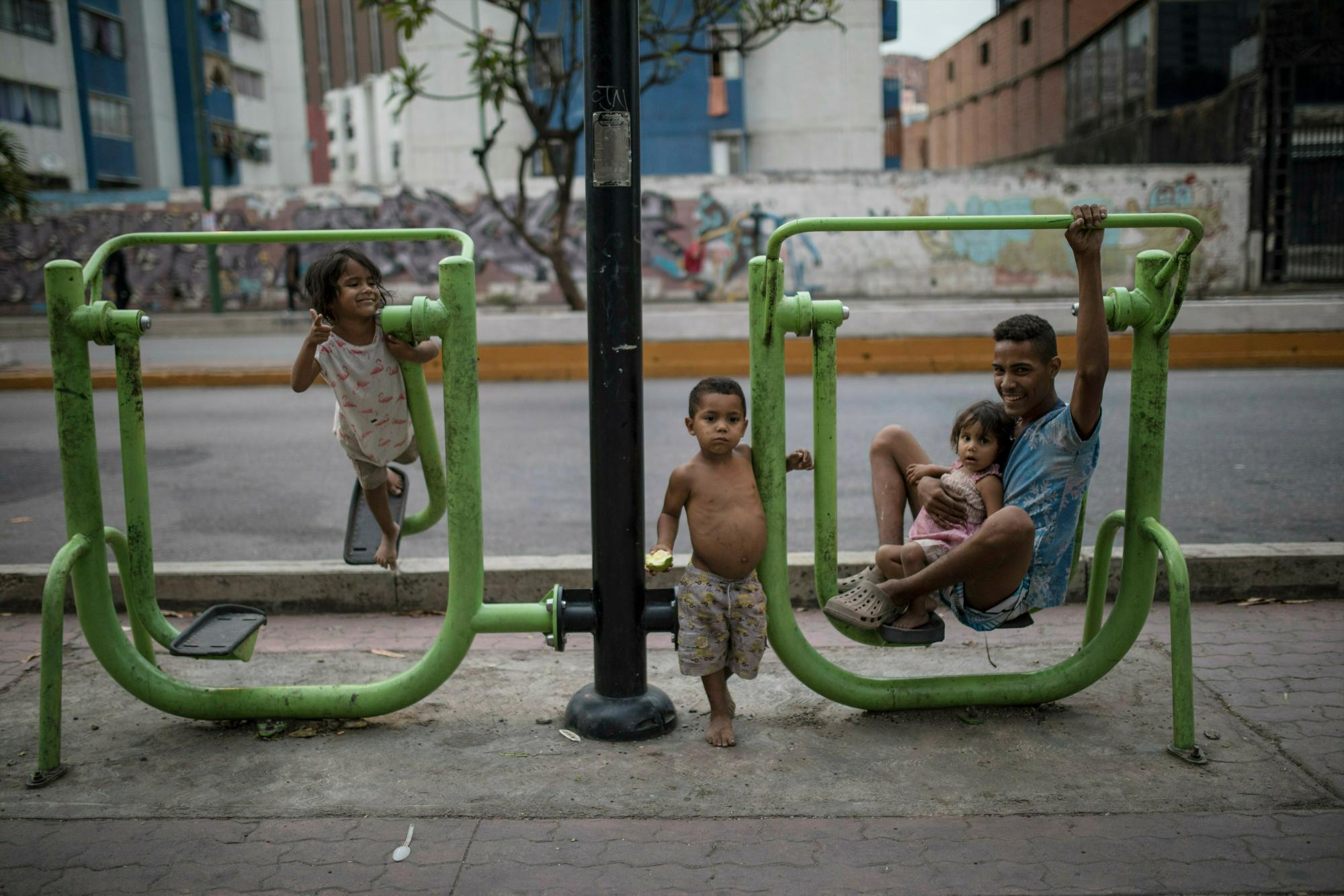 Un hombre descansa en equipos de gimnasia al aire libre mientras cuida a los niños en un patio de recreo público en Caracas, Venezuela, el lunes 13 de mayo de 2019.  Los funcionarios de la administración de los Estados Unidos han advertido que se espera que 2 millones más huyan a finales de año si la crisis continúa en la nación rica en petróleo.