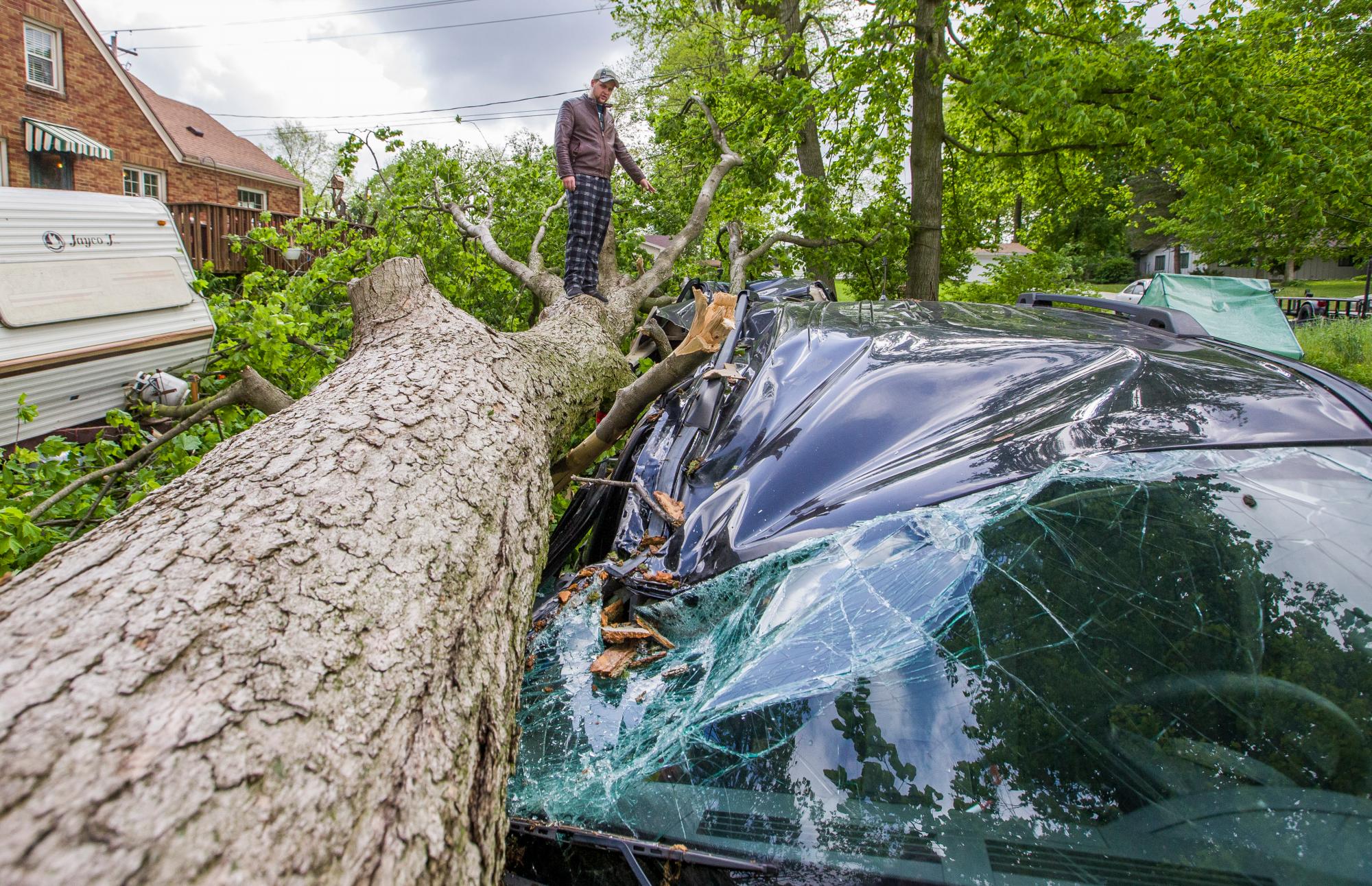 Michael Clark se sube a un árbol derribado para comprobar el daño a tres vehículos en su casa el jueves 23 de mayo de 2019, en South Bend, Indiana donde fuertes vientos y tormentas causaron daños y apagones en muchas áreas durante la noche.