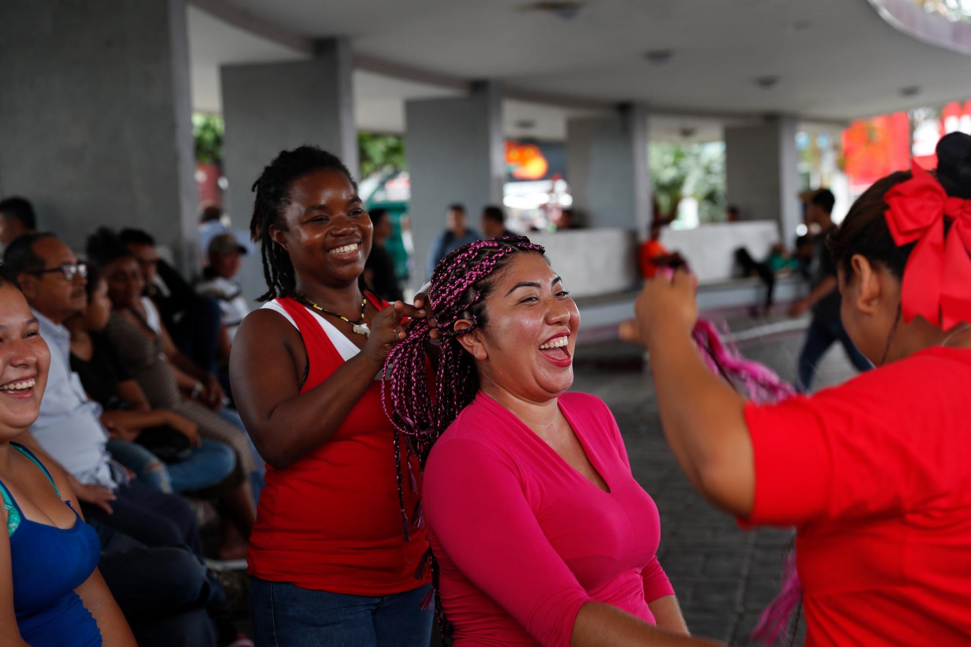 Las migrantes hondureños hacen trenzas al cabello de los demás en la plaza principal de Tapachula, México, el domingo 2 de junio de 2019.