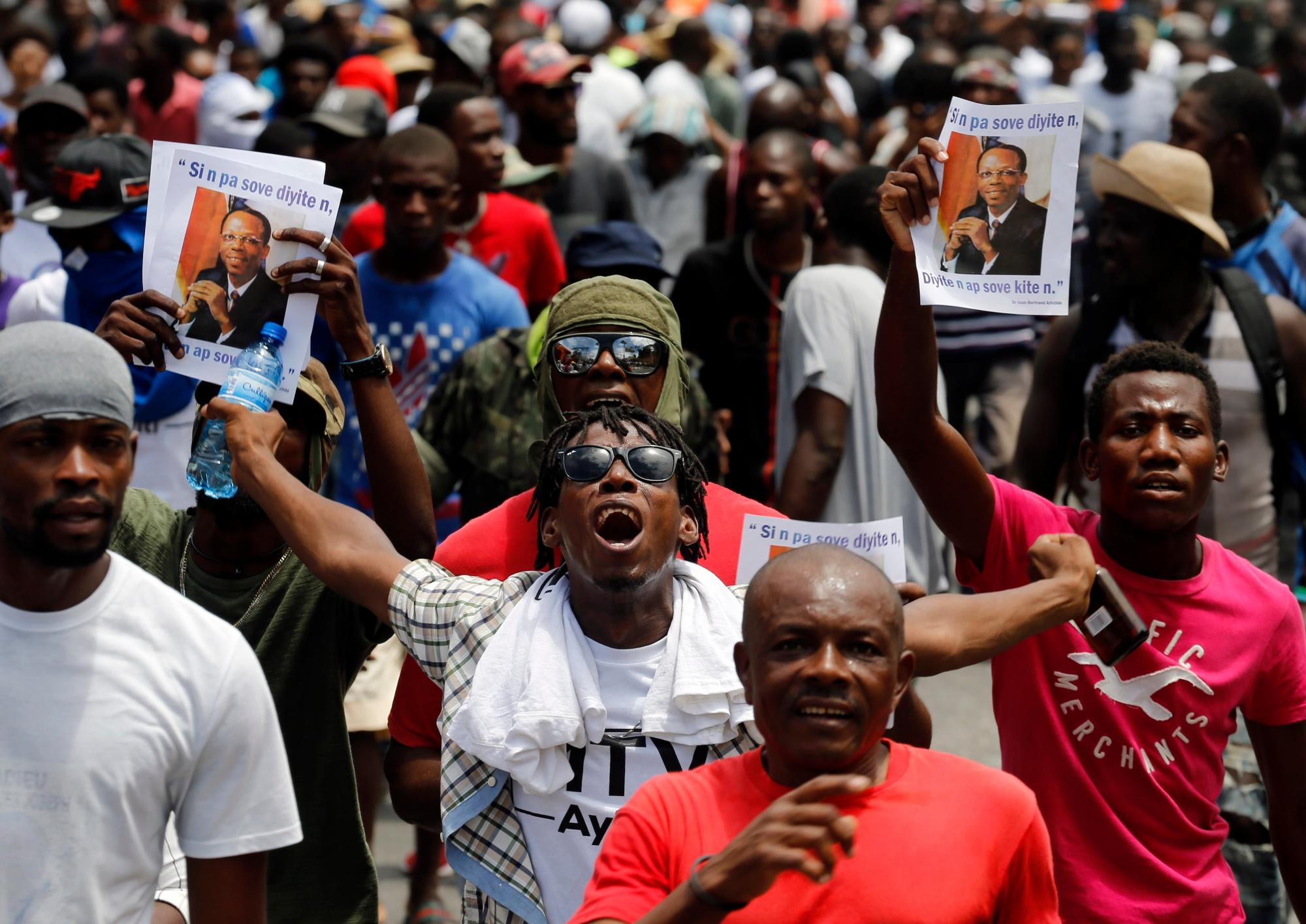 Un manifestante grita los lemas antigubernamentales, ya que otros tienen imágenes del ex Presidente Jean-Bertrand Aristide en Puerto Príncipe, Haití, el domingo 9 de junio de 2019. Los manifestantes denunciando la corrupción paralizaron gran parte de la capital, ya que exigían la destitución del Presidente Jovenel Moise. 