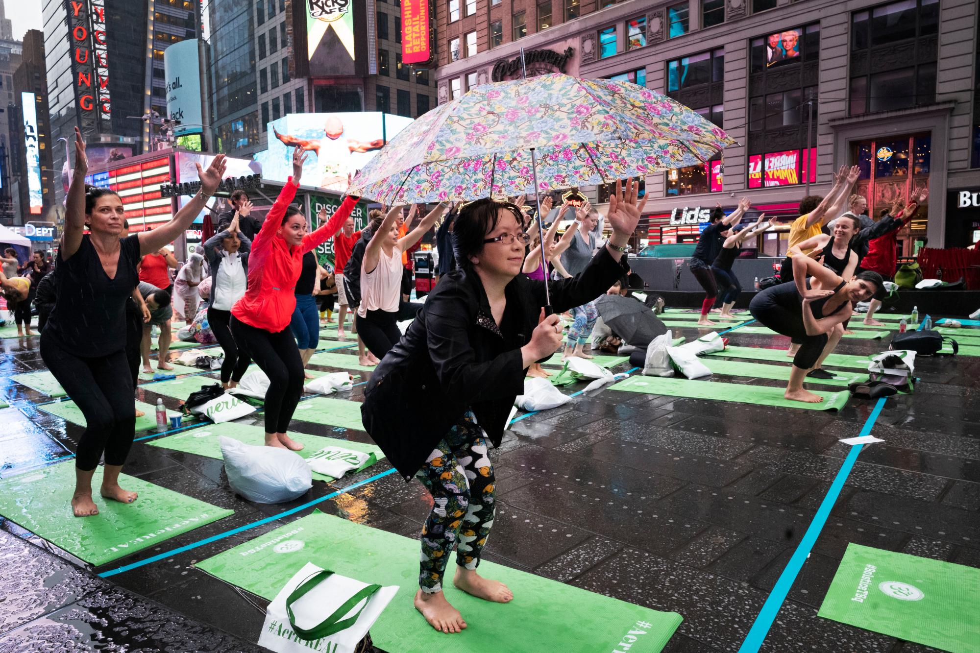 Una mujer con un paraguas participa en el evento de yoga Mind Over Madness para celebrar el solsticio de verano durante una tormenta en el Times Square de Nueva York, el viernes 21 de junio de 2019. 