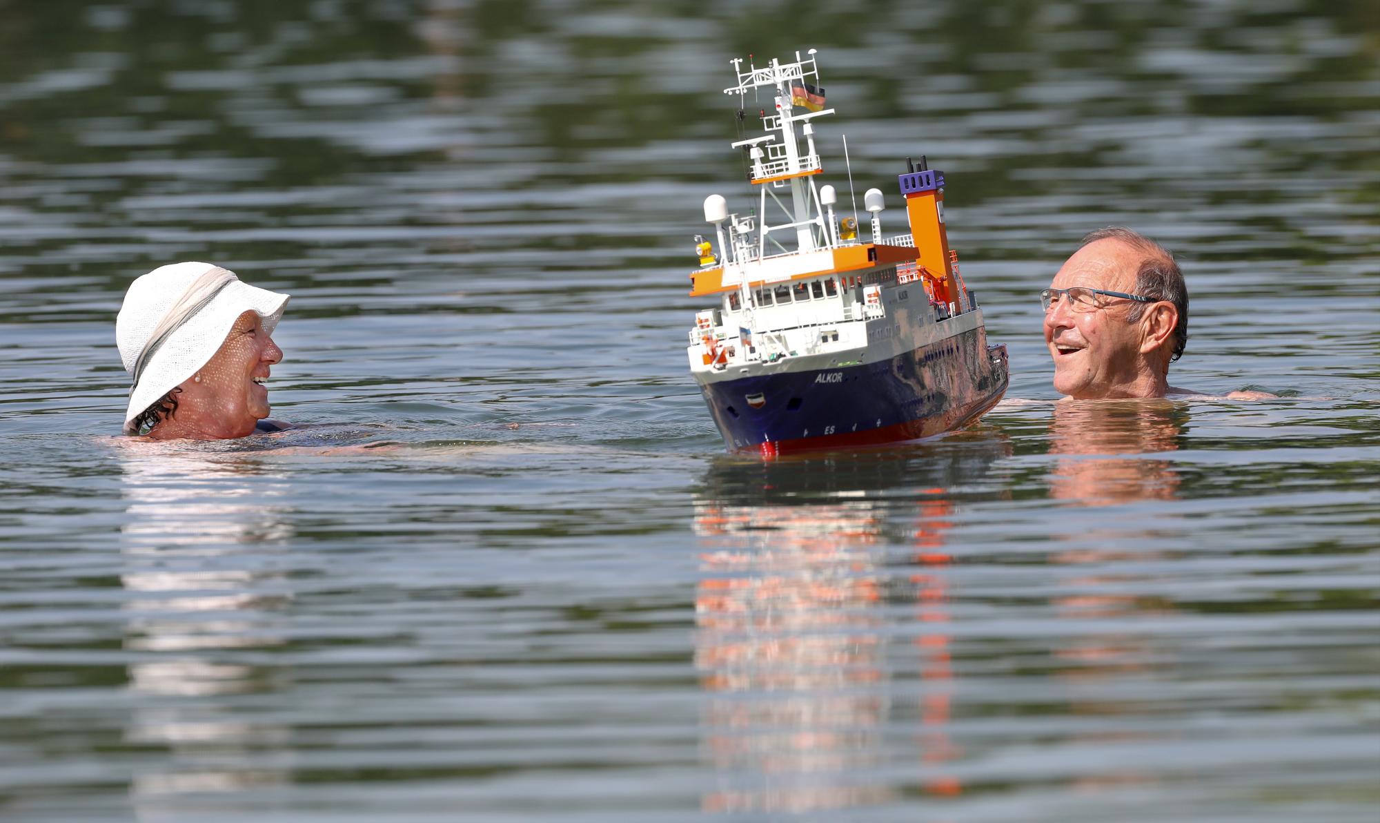 Una pareja nada junto a un modelo de barco en un lago en Ertingen, Alemania, el miércoles 26 de junio de 2019. Una ola de calor golpea a Alemania y Europa con temperaturas cercanas a los 40 grados centígrados. 