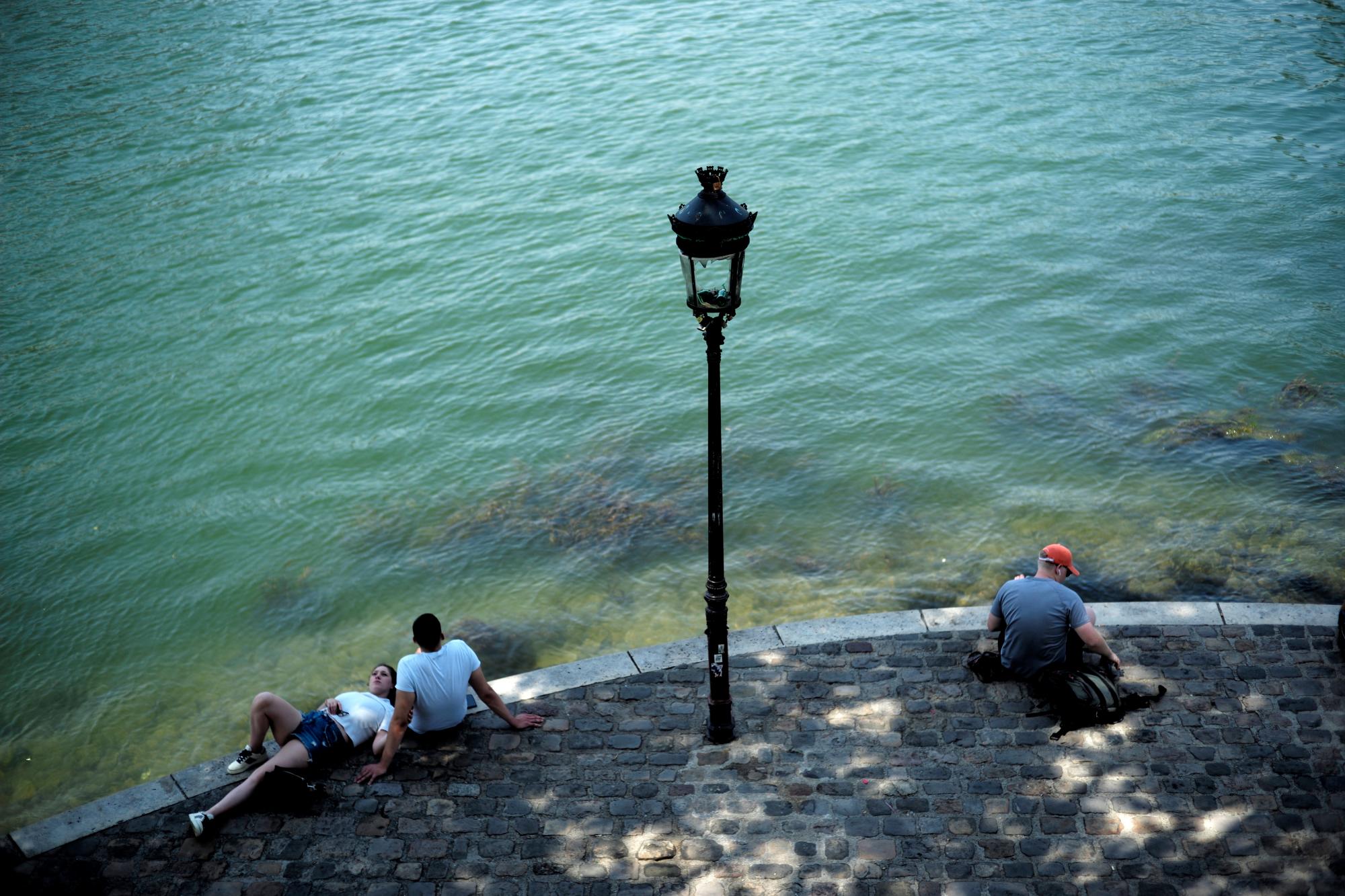 La gente descansa a lo largo del río Sena el miércoles 26 de junio de 2019 en París. Se espera que las altas temperaturas suban a 39 grados centígrados (102 grados Fahrenheit) en el área de París a fines de esta semana y que calienten gran parte del país, desde los Pirineos en el suroeste hasta la frontera alemana en el noreste. 