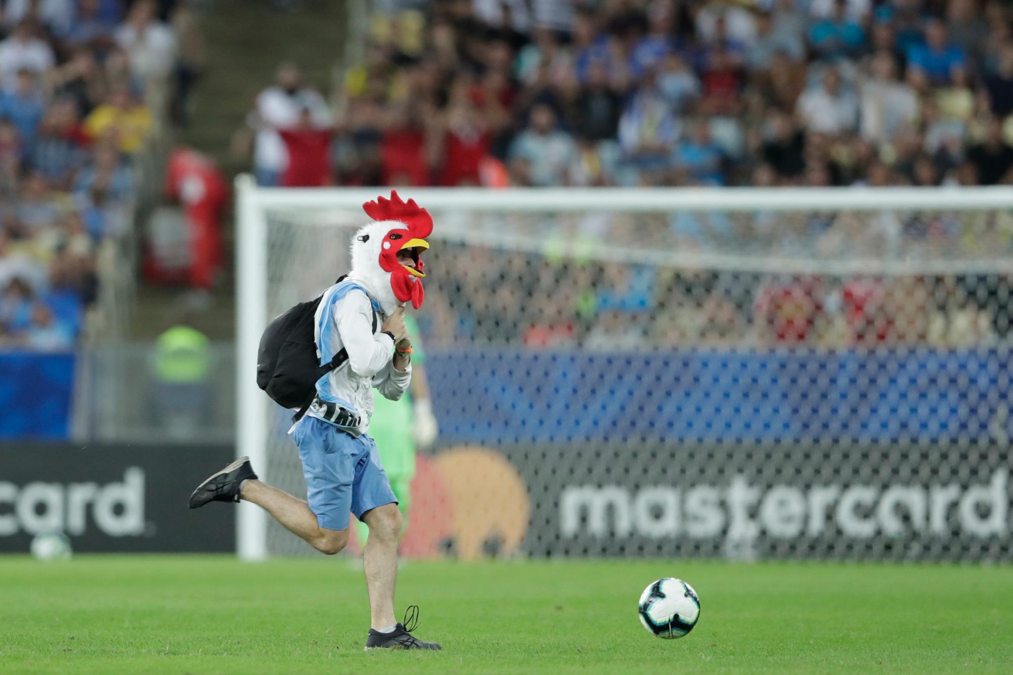 En esta imagen, tomada el 24 de junio de 2019, un aficionado con una máscara de gallo corre por el campo durante un partido del Grupo C de la Copa América entre Chile y Uruguay, en el estadio de Maracaná, en Río de Janeiro, Brasil. 
