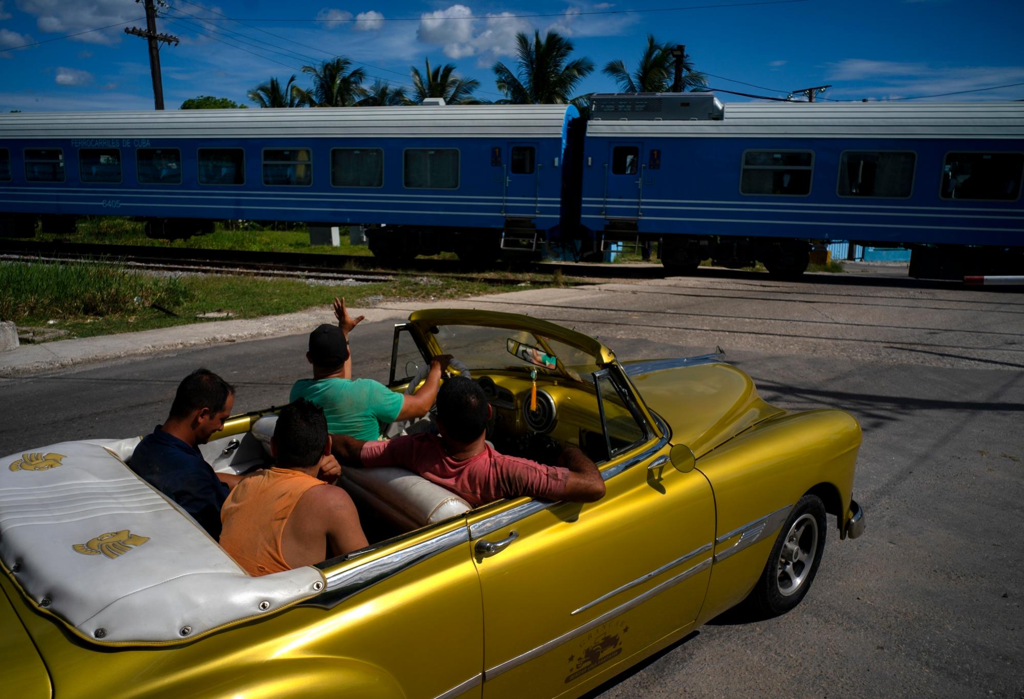 Un conductor de un automóvil clásico estadounidense hace olas cuando el primer tren con equipo nuevo de China pasa por el pasado, en La Habana, Cuba, el sábado 13 de julio de 2019. El primer tren con equipo nuevo de China salió de La Habana el sábado, transportando pasajeros en el El inicio de un viaje de 915 kilómetros (516 millas) hacia el extremo oriental de la isla mientras el gobierno trata de revisar el sistema ferroviario decrépito y envejecido del país. 