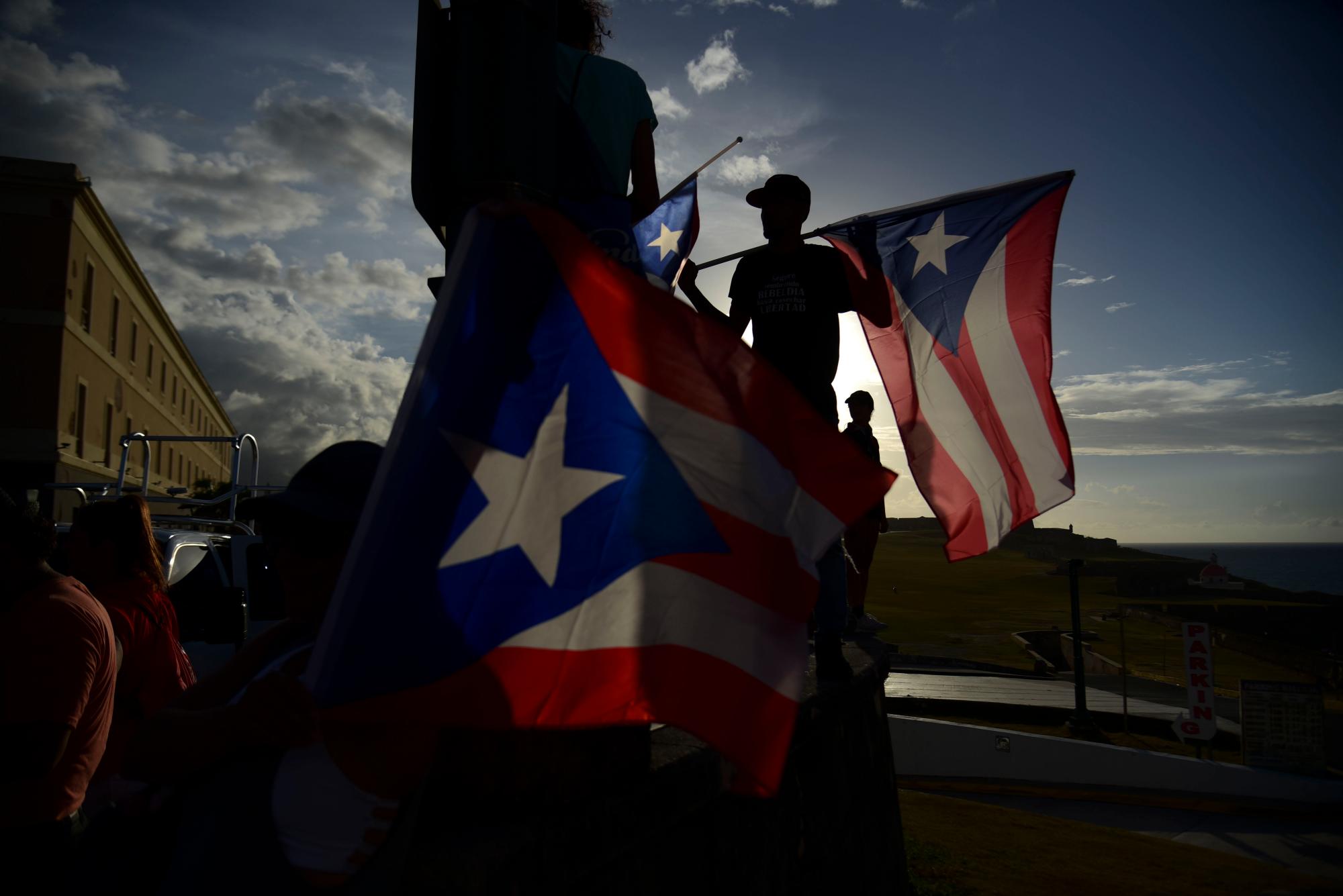 Los manifestantes sostienen banderas de Puerto Rico cuando se reúnen en la Plaza Quinto Centenario para protestar contra el gobernador Ricardo Rossello, en San Juan, Puerto Rico, el miércoles 17 de julio de 2019. 