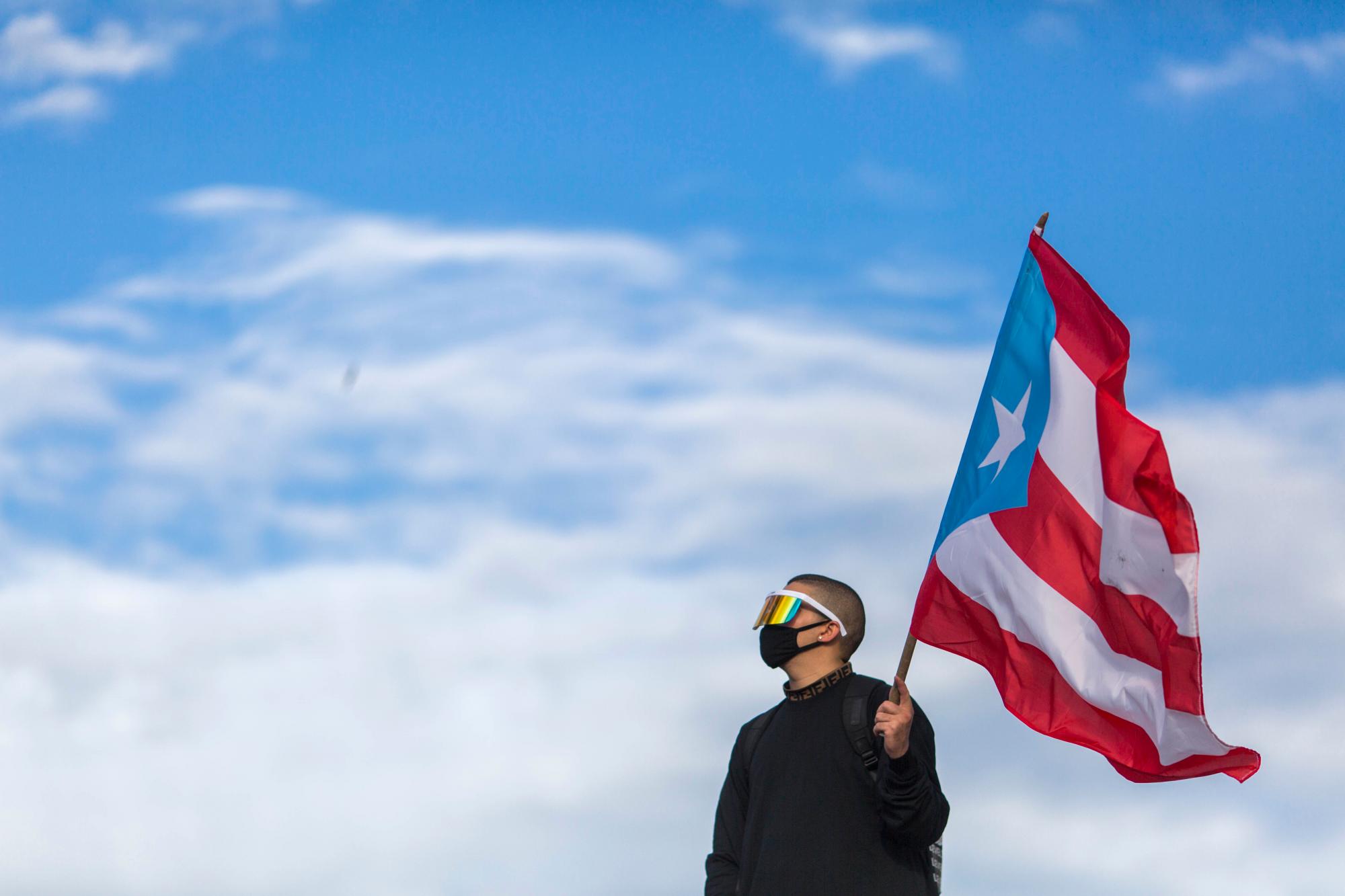 El cantante de trap latino y de reggaeton Benito Antonio Martínez Ocasio, conocido por su nombre artístico de Bad Bunny, sostiene una bandera de Puerto Rico antes de una marcha de protesta contra el gobernador Ricardo Rosello, en San Juan, Puerto Rico, el miércoles 17 de julio de 2019.