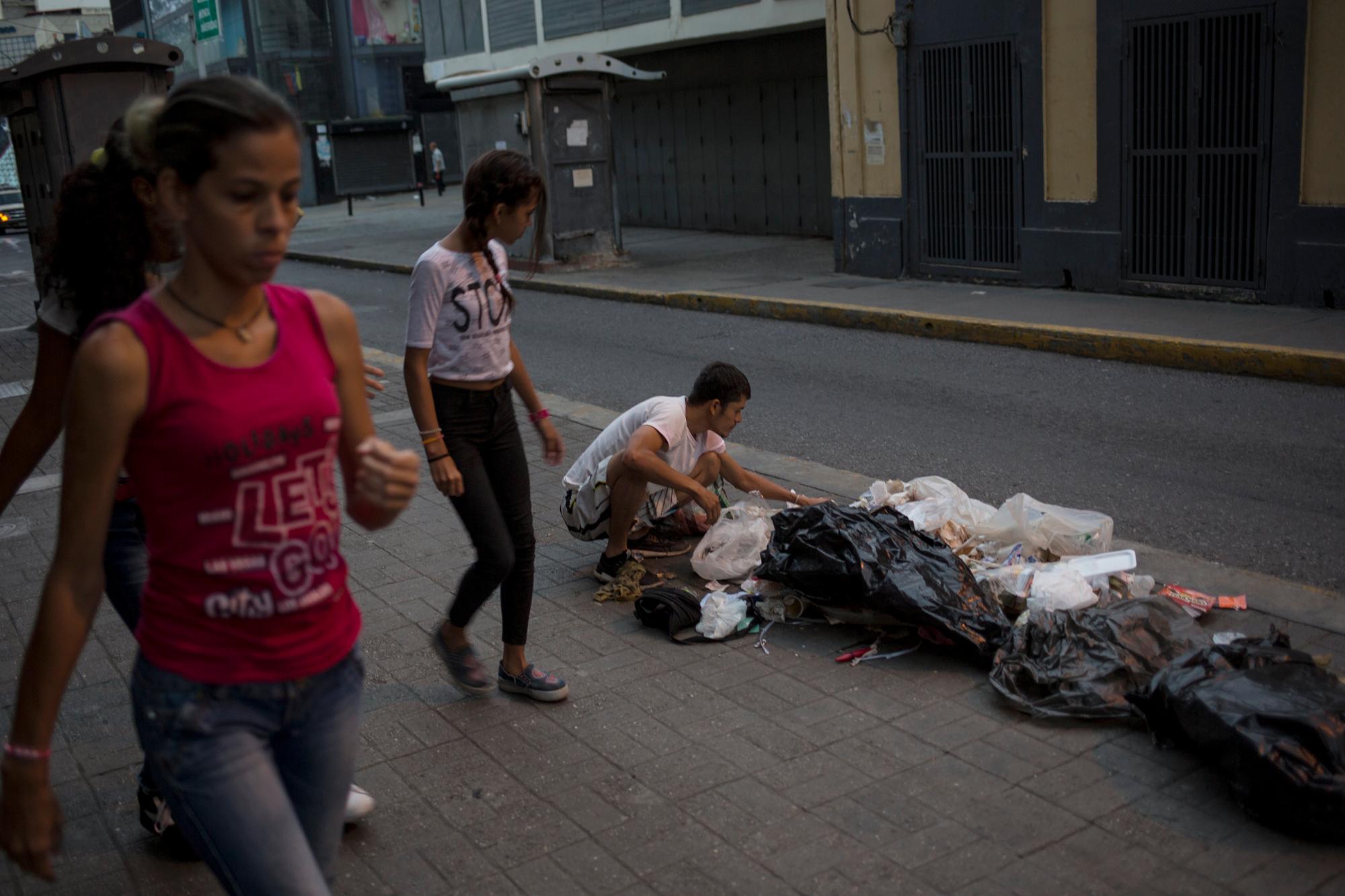 En esta fotografía del martes 16 de julio de 2019, Kevin González buca comida entre la basura en una acera de Caracas, Venezuela. 