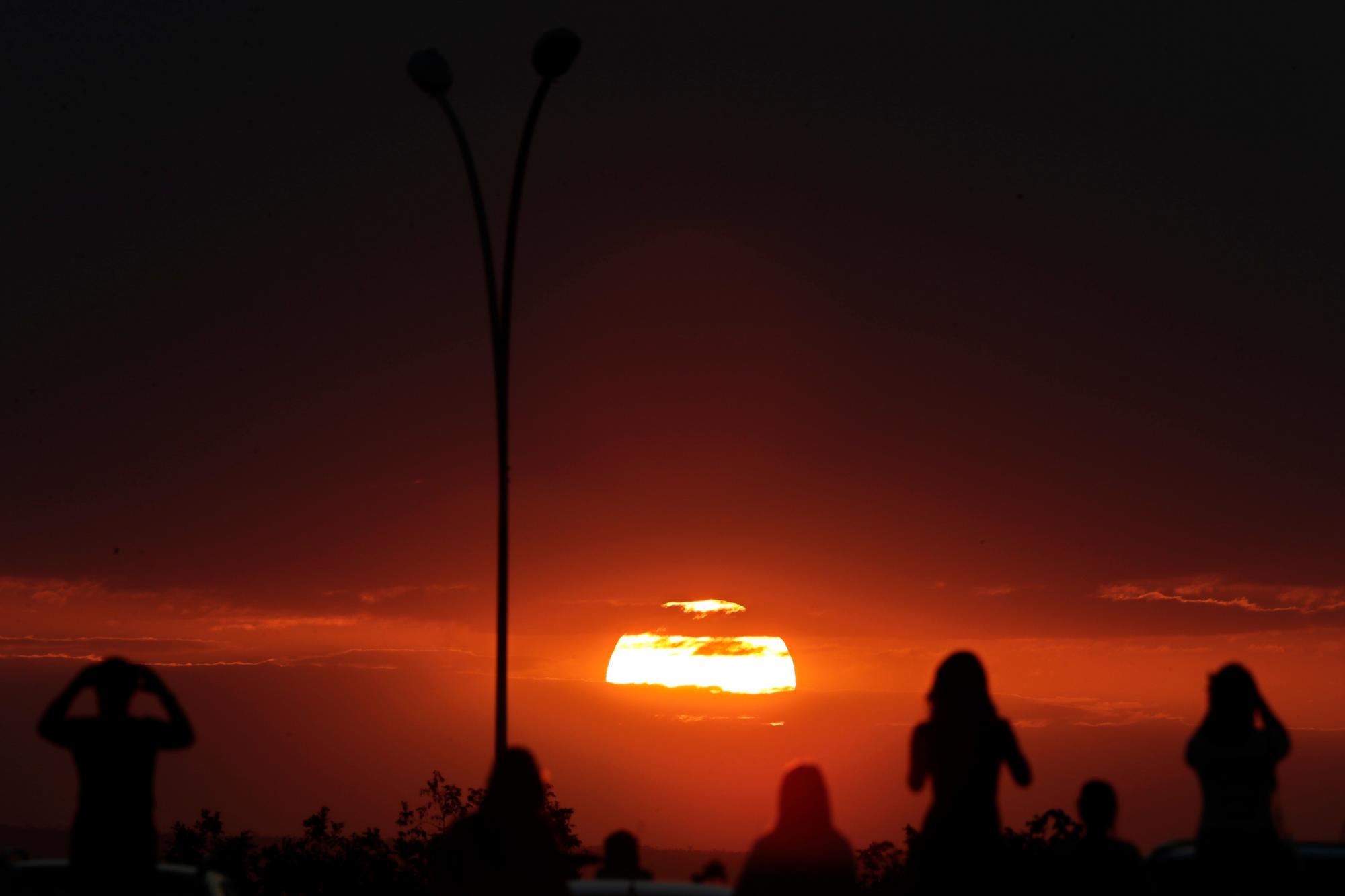 En esta fotografía del martes 16 de julio de 2019, varias personas observan la puesta de sol antes de un eclipse lunar parcial en los cielos de Brasilia, Brasil. 