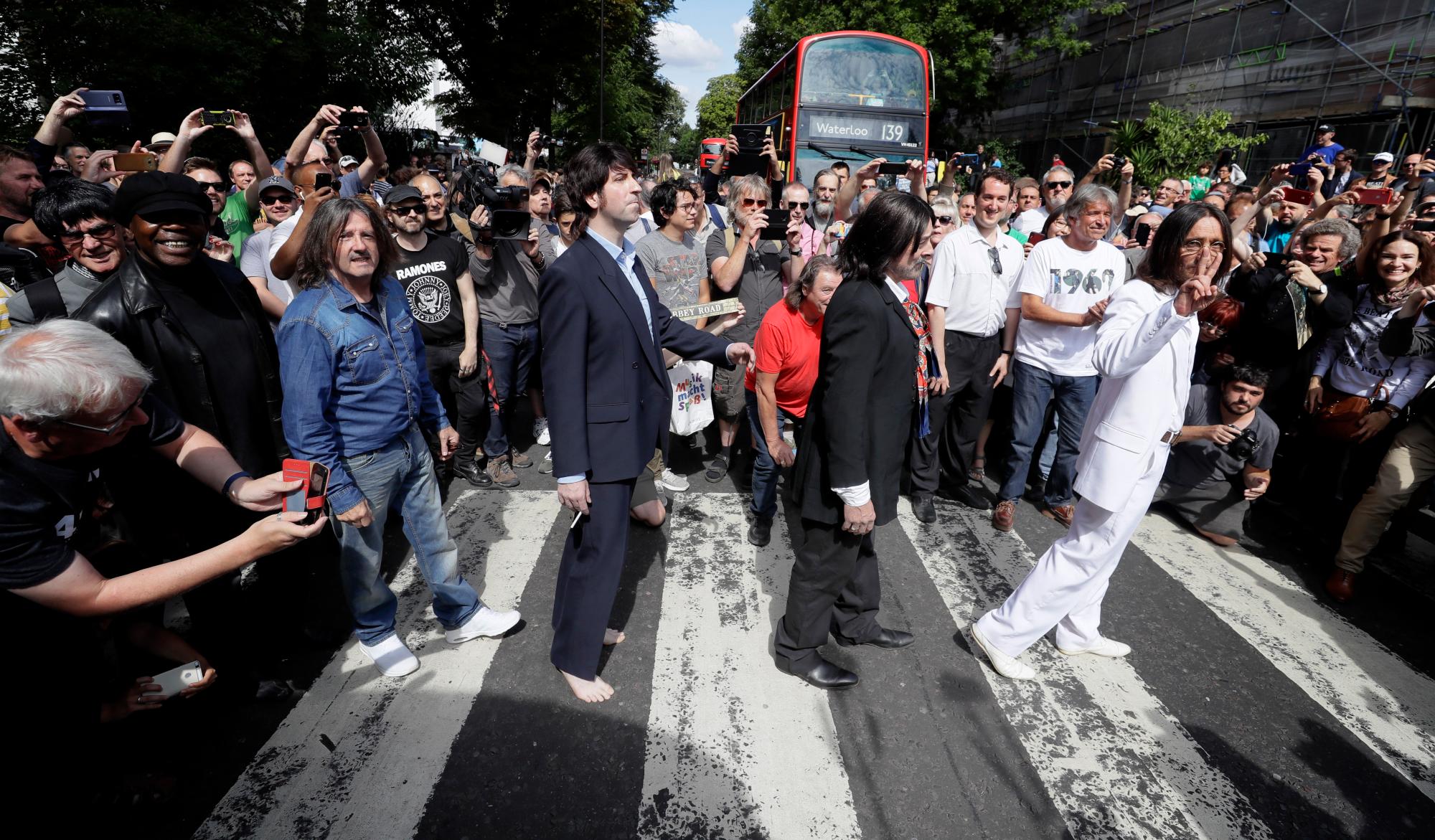 Los fanáticos vestidos como parecidos caminan por el paso de cebra de Abbey Road en el 50 aniversario de los músicos pop británicos The Beatles haciéndolo para la portada de su álbum ‘Abbey Road’ en St Johns Wood en Londres, jueves, agosto. 8, 2019. Su objetivo era cruzar 50 años al minuto desde que los ‘Fab Four’ fueron fotografiados para el álbum.