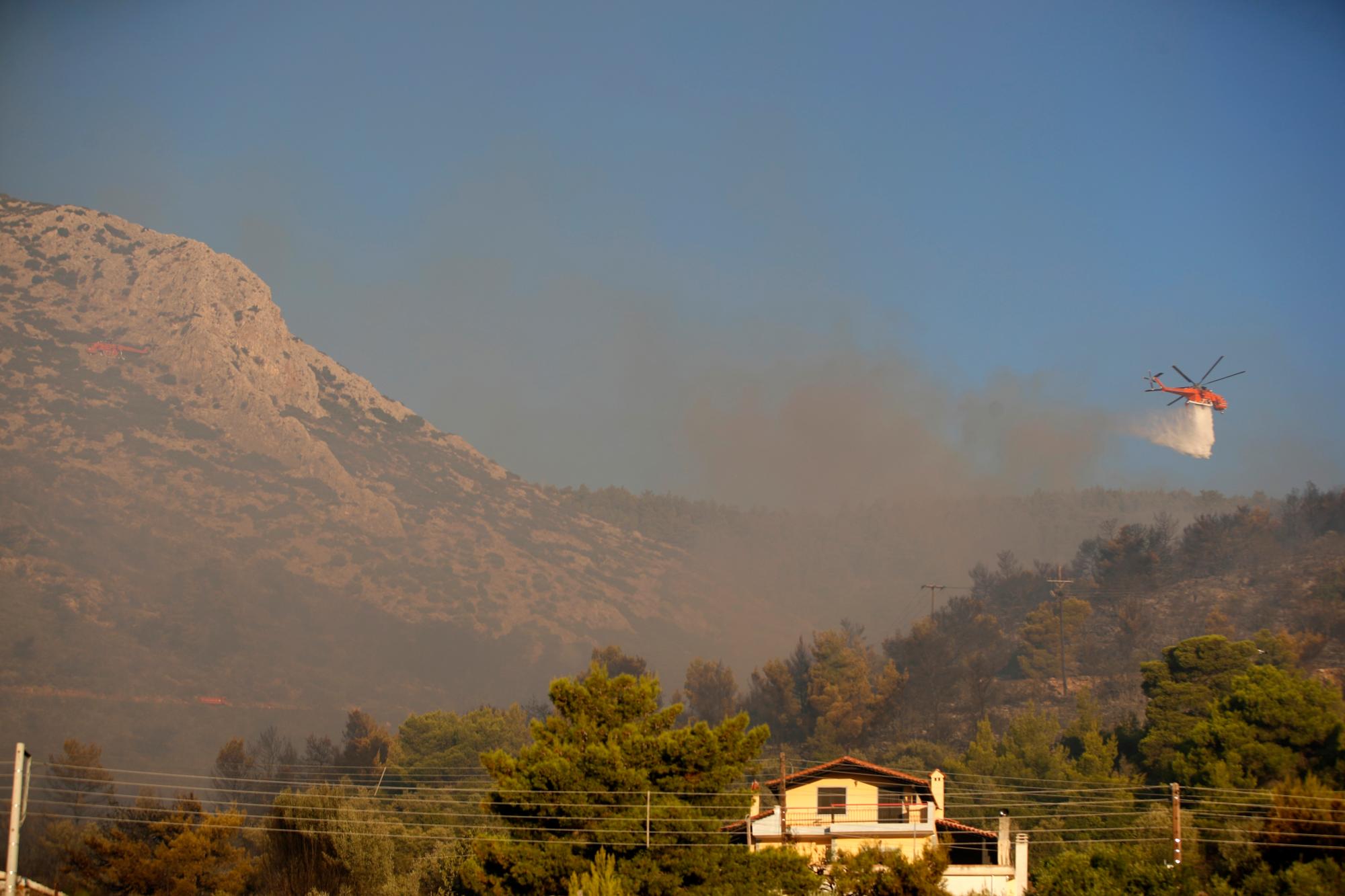 Un helicóptero arroja agua sobre un incendio en Peania, en el este de Atenas, el lunes 12 de agosto de 2019. Se produjo un gran incendio en el suburbio de Peania en Atenas, al este de la ciudad, y las autoridades ordenaron la evacuación de las casas cercanas. 