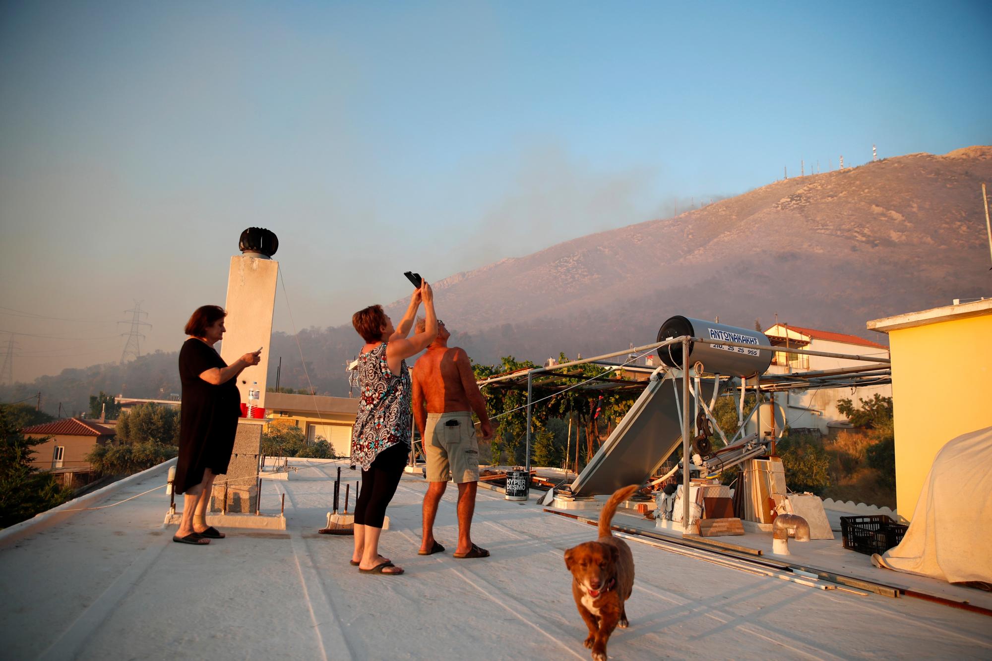 Los residentes locales miran un incendio forestal desde una azotea en Peania, al este de Atenas, el lunes 12 de agosto de 2019. Se produjo un gran incendio en el suburbio de Peania en Atenas, al este de la ciudad, y las autoridades ordenaron la evacuación de las casas cercanas. 