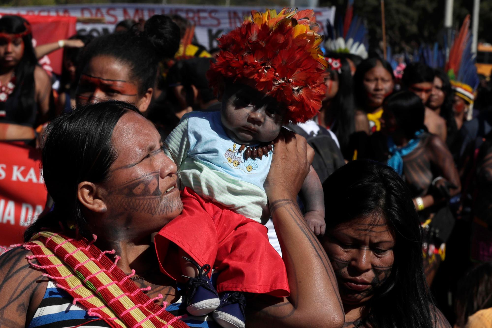 Una madre indígena lleva a su hijo durante la Marcha de la Salud de las Mujeres Indígenas, en Brasilia, Brasil, el lunes 12 de agosto de 2019. Las mujeres indígenas con vestimenta tradicional y caras pintadas participan en un campamento de varios días en Brasilia con el objetivo de resaltar los problemas de los derechos indígenas. 
