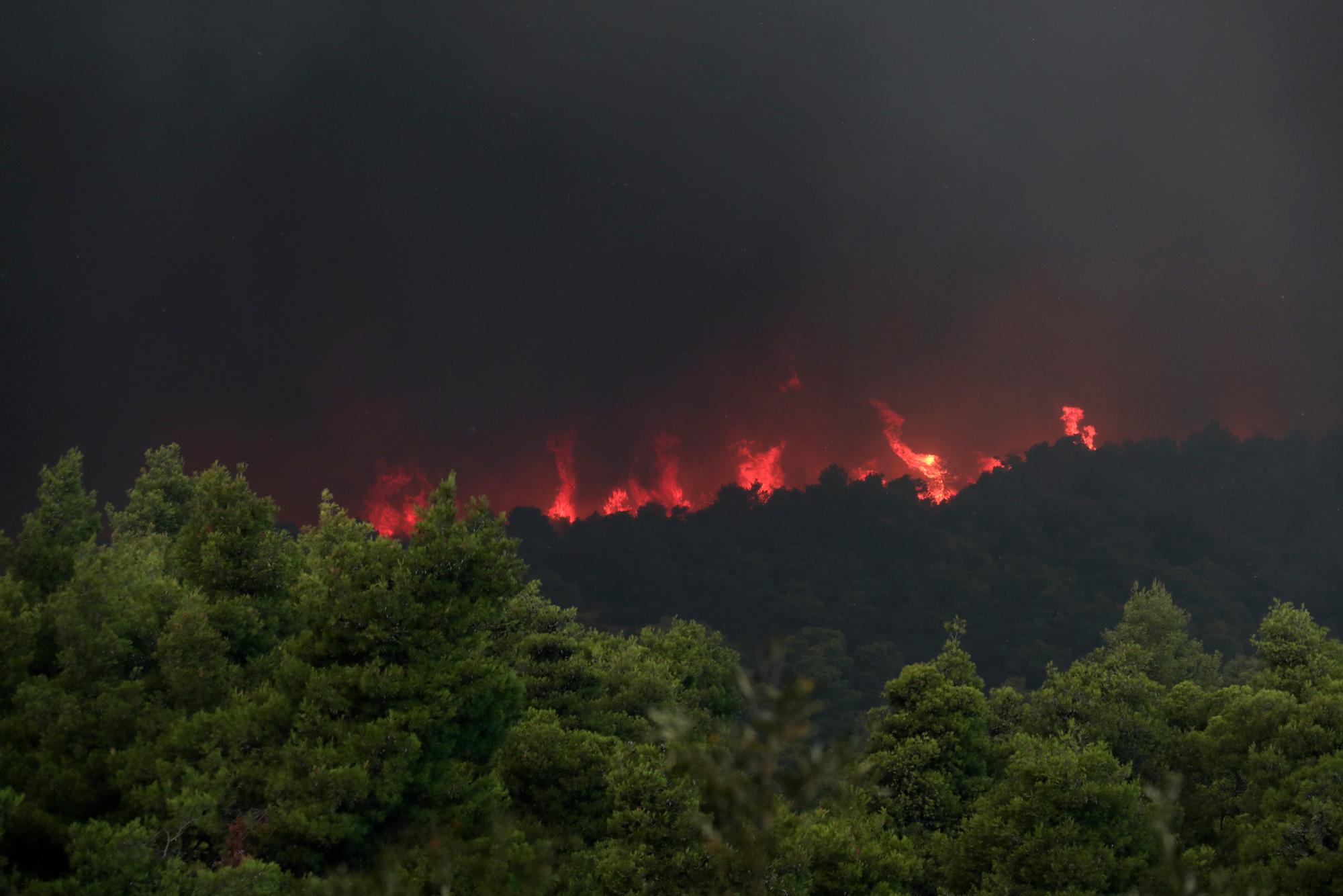 Las llamas se elevan desde un incendio forestal cerca de la aldea de Psachna en la isla de Evia, al noreste de Atenas, el martes 13 de agosto de 2019. Docenas de bomberos respaldados por aviones que arrojan agua están luchando contra un incendio forestal en la isla que dejó la capital griega cubierta en humo. 