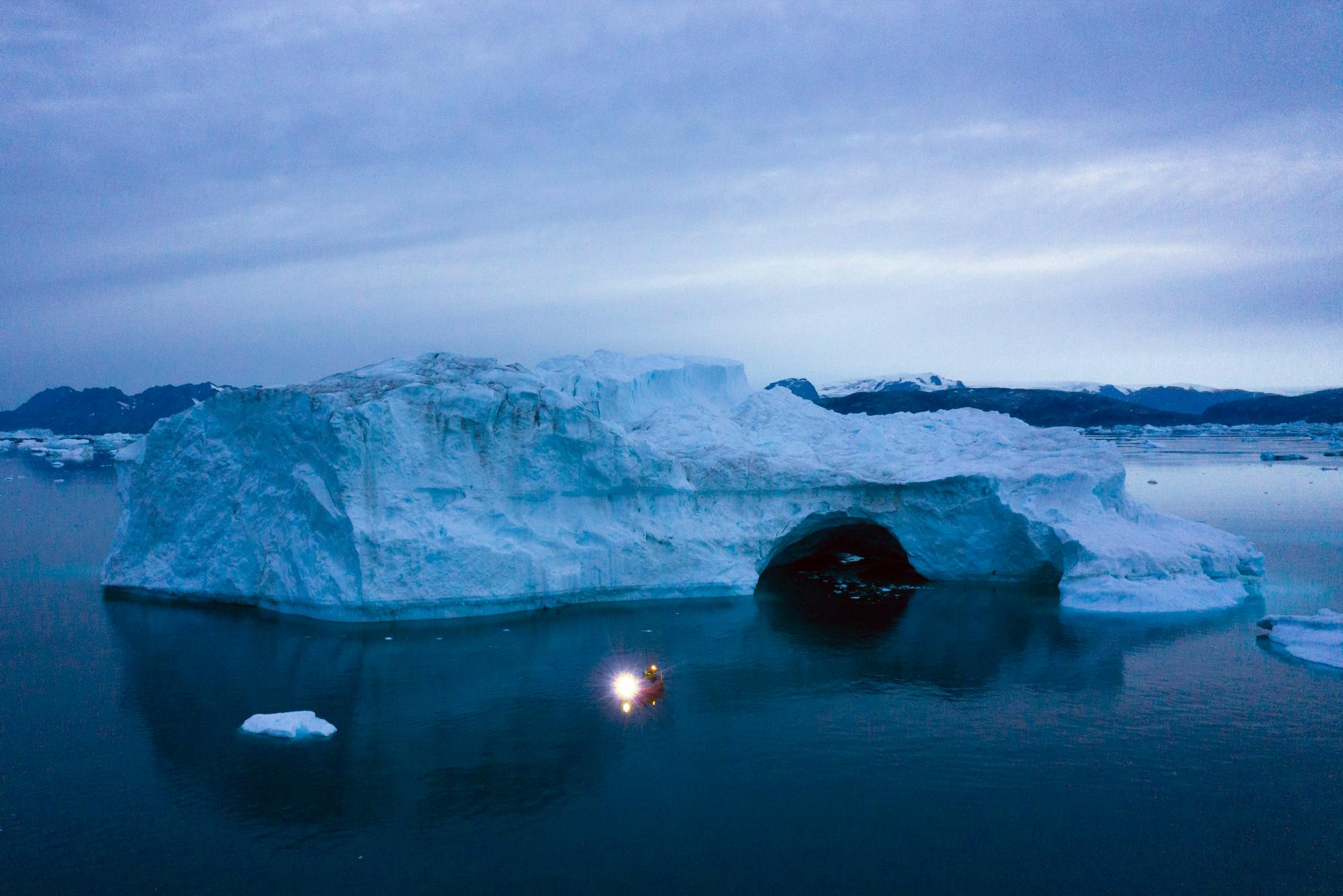 A boat navigates at night next to a large iceberg in eastern Greenland, late Friday, Aug. 15, 2019. Greenland has been melting faster in the last decade and this summer, it has seen two of the biggest melts on record since 2012. 