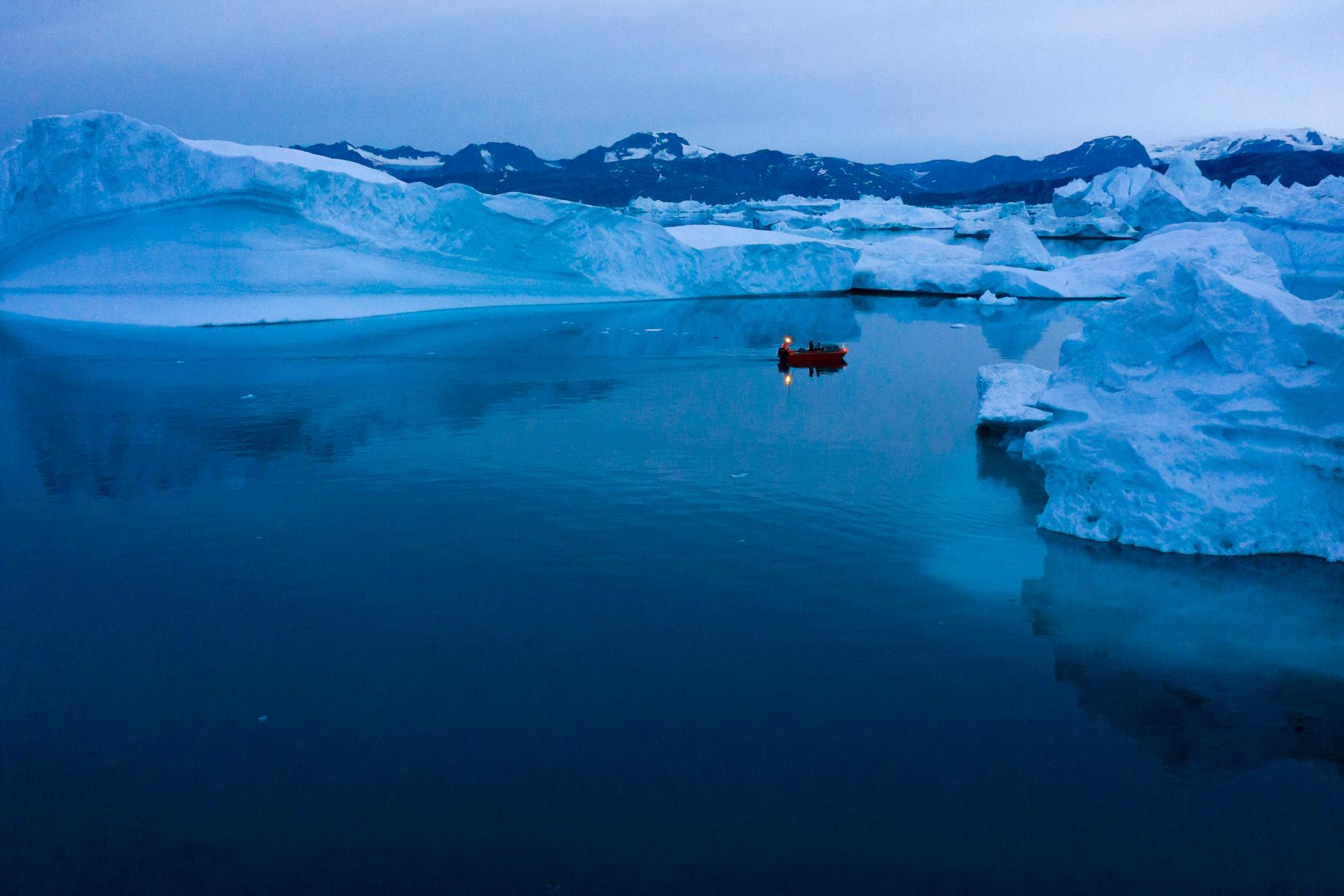 Un barco navega por la noche entre icebergs en el este de Groenlandia, a última hora del viernes 15 de agosto de 2019. Groenlandia se ha derretido más rápido en la última década y este verano, ha visto dos de los derretimientos más grandes registrados desde 2012.