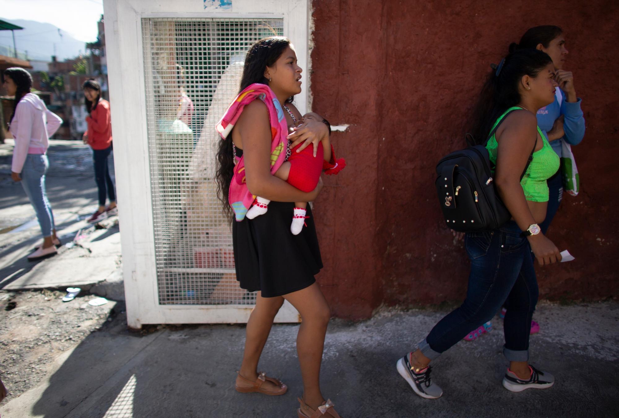 En esta foto tomada el 25 de julio de 2019, Nicol Ramírez, de 15 años, lleva a su bebé a una clínica donde espera recibir un implante hormonal para prevenir futuros embarazos en el barrio de Caucaguita, en las afueras de Caracas, Venezuela. Ramírez y su hermana estuvieron entre los pocos afortunados que recibieron el último implante después de que su madre pagó una prueba de embarazo y pudieron demostrar que no estaban embarazadas. 