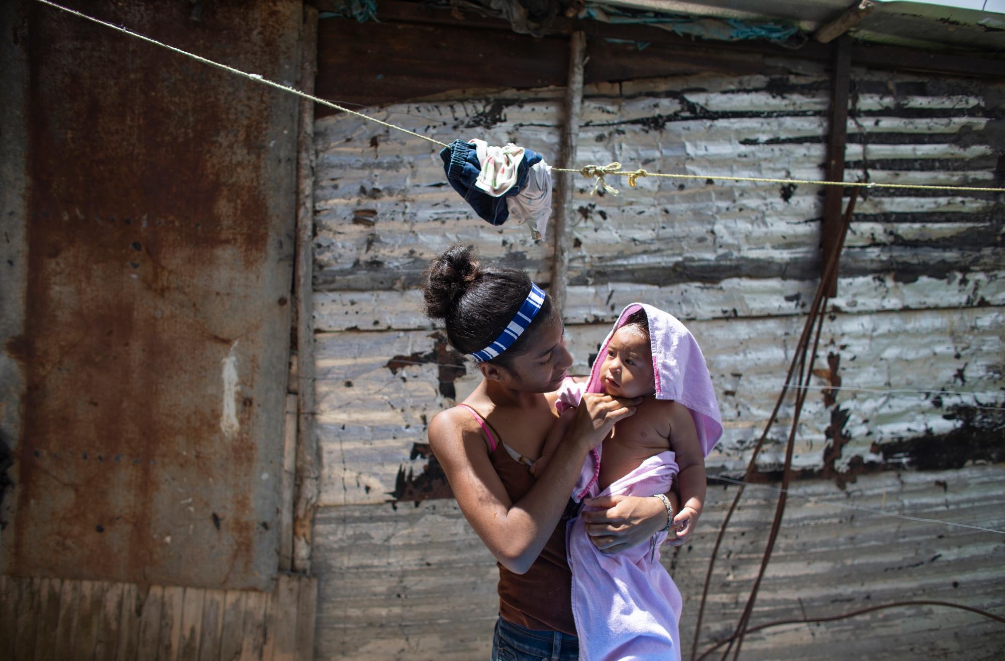 En esta foto tomada el 25 de julio de 2019, Karelys Herrera, de 15 años, sostiene a su bebé después de bañarlo detrás de su casa en el barrio de Caucaguita, en las afueras de Caracas, Venezuela. Herrera dijo que contemplaba el suicidio después de enterarse de que estaba embarazada a los 14 años. 
