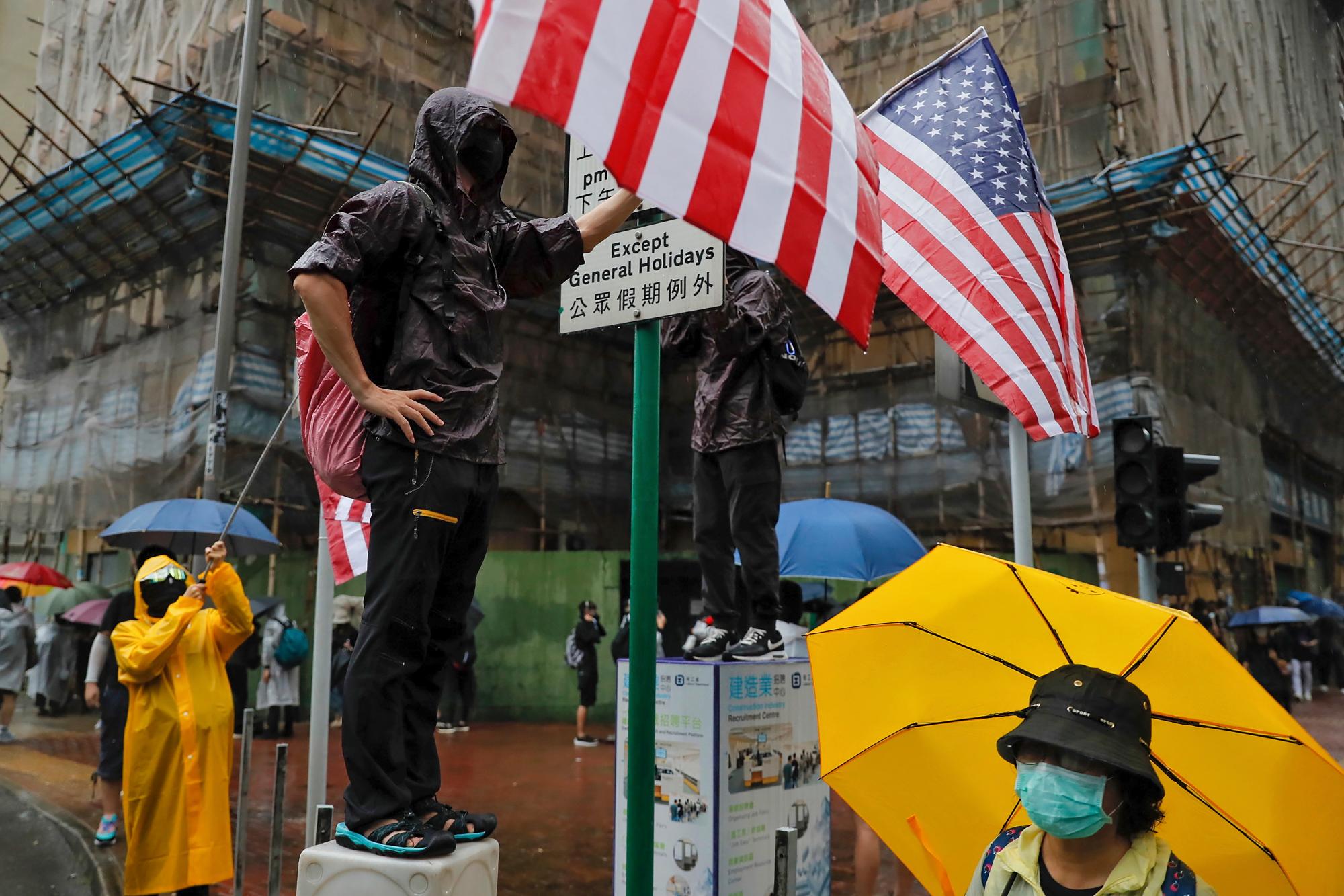 Un manifestante sostiene banderas estadounidenses mientras se enfrentan a la policía antidisturbios durante una protesta en Hong Kong, el domingo 25 de agosto de 2019. La policía se enfrenta con los manifestantes en Hong Kong por segundo día consecutivo el domingo después de una marcha a favor de la democracia en un distrito periférico. 