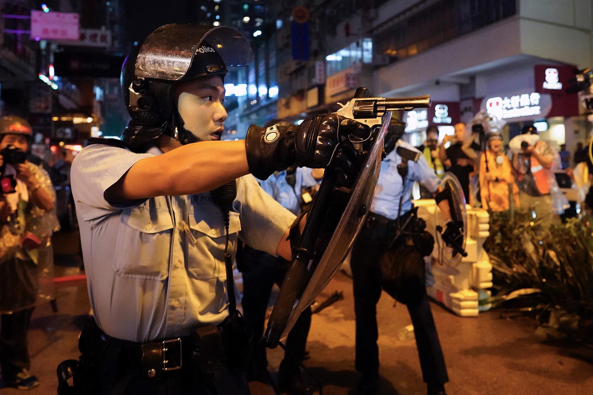 Un policía apunta un arma durante una protesta en Hong Kong, el domingo 25 de agosto de 2019. La policía de Hong Kong ha lanzado camiones de cañones de agua por primera vez en las protestas prodemocráticas de este verano. Los dos camiones avanzaron con los agentes antidisturbios el domingo por la noche mientras empujaban a los manifestantes a lo largo de una calle en el distrito periférico de Tsuen Wan. 
