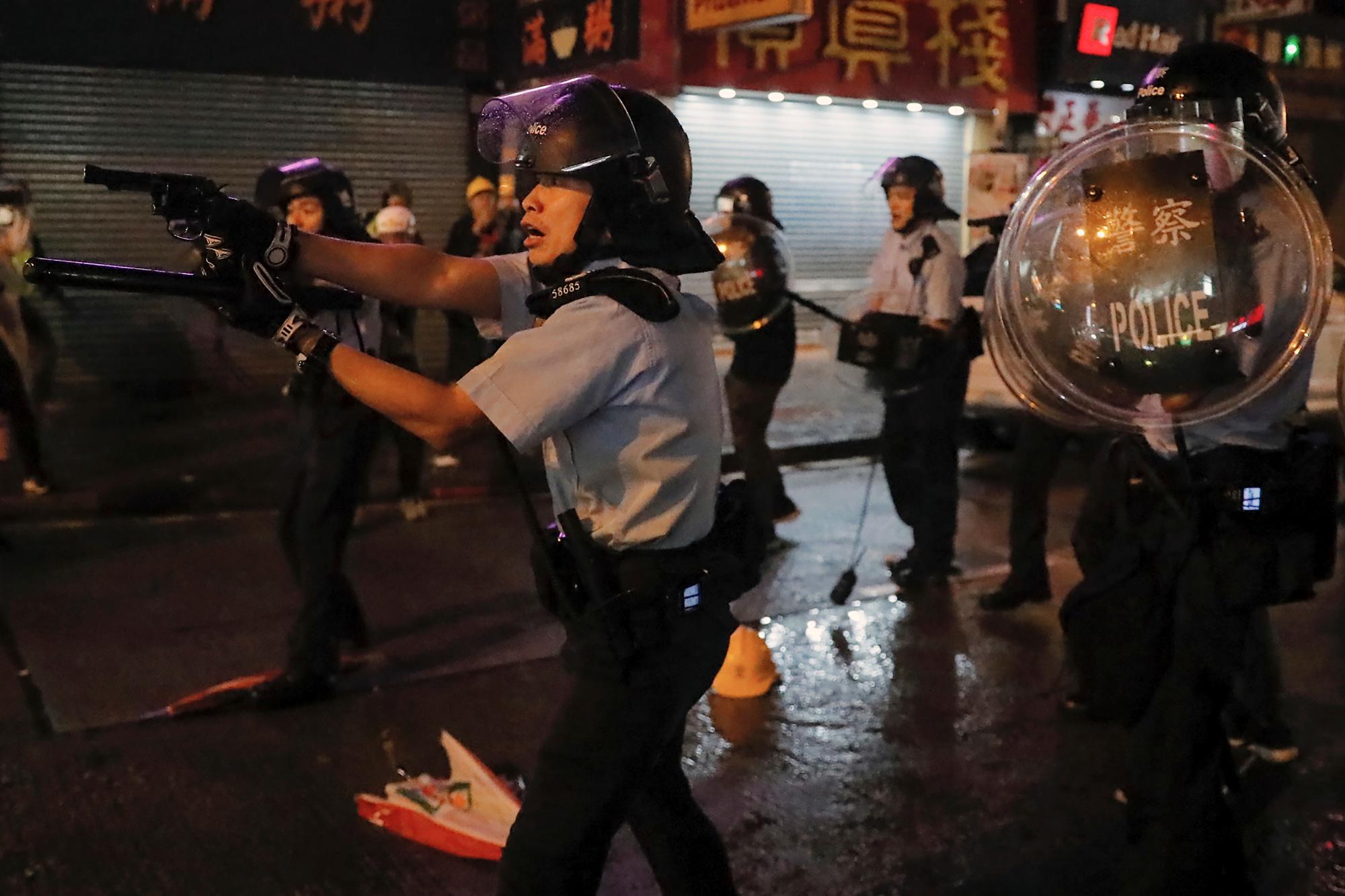 Un policía apunta su arma hacia los manifestantes en una calle durante una protesta en Hong Kong, el domingo 25 de agosto de 2019. La policía de Hong Kong ha lanzado camiones de cañones de agua por primera vez en las protestas prodemocráticas de este verano. Los dos camiones avanzaron con los agentes antidisturbios el domingo por la noche mientras empujaban a los manifestantes a lo largo de una calle en el distrito periférico de Tsuen Wan. 