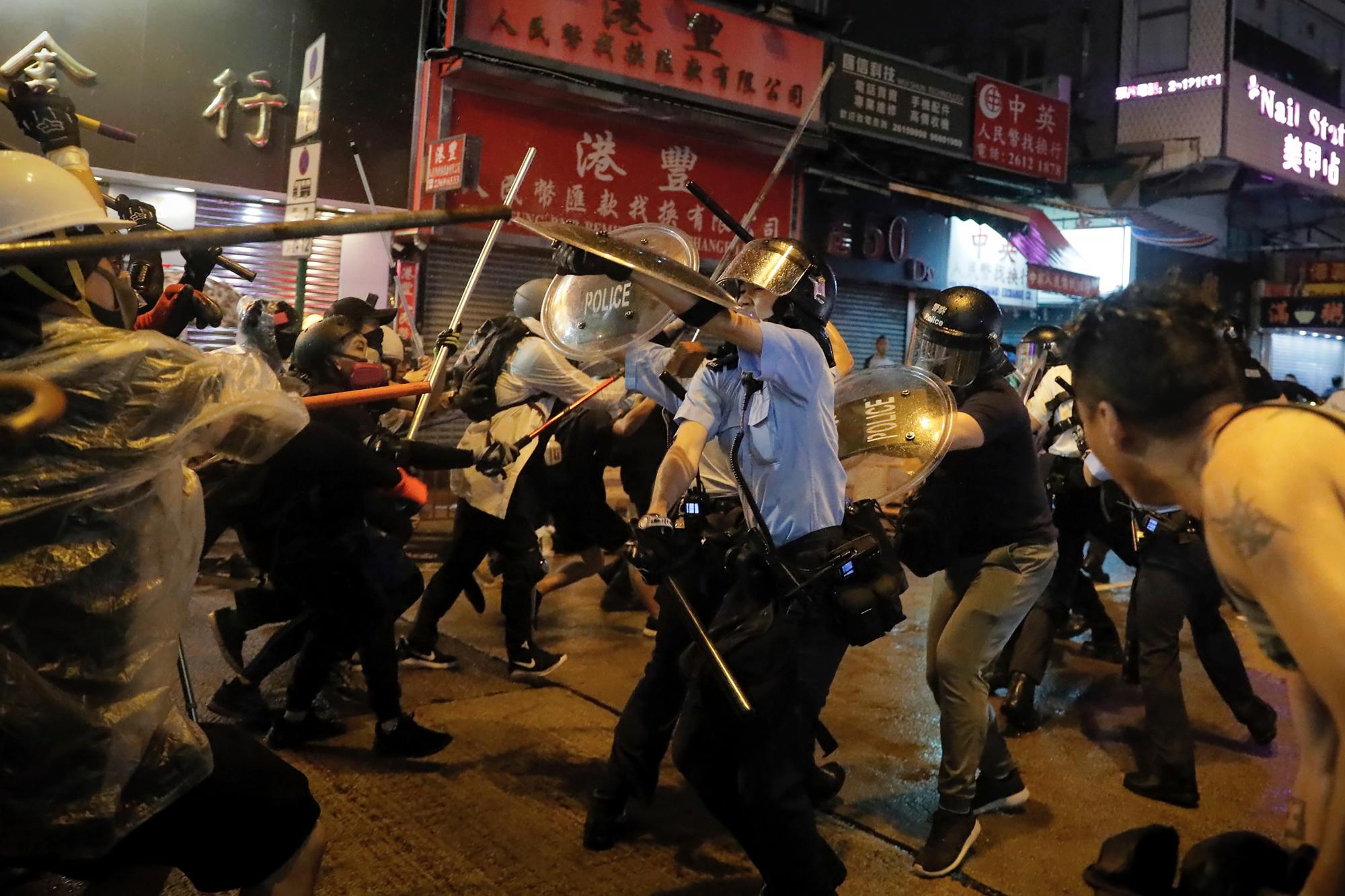 Los policías chocan con los manifestantes en una calle durante una protesta en Hong Kong, el domingo 25 de agosto de 2019. La policía de Hong Kong ha usado camiones de cañones de agua por primera vez en las protestas en favor de la democracia de este verano. Los dos camiones avanzaron con los agentes antidisturbios el domingo por la noche mientras empujaban a los manifestantes a lo largo de una calle en el distrito periférico de Tsuen Wan.