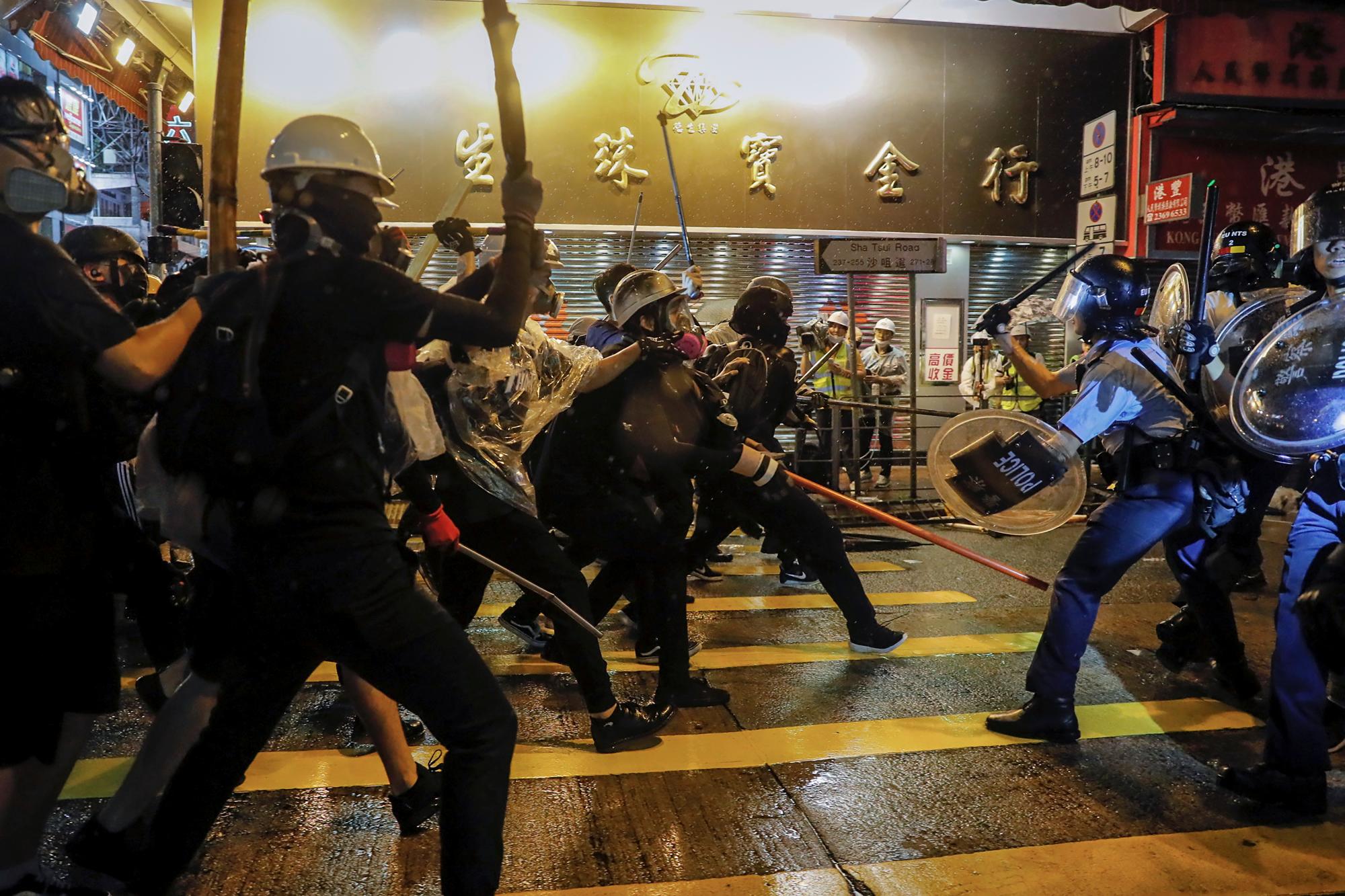 Los policías chocan con los manifestantes en una calle durante una protesta en Hong Kong, el domingo 25 de agosto de 2019. La policía de Hong Kong ha lanzado camiones de cañones de agua por primera vez en las protestas en favor de la democracia de este verano. Los dos camiones avanzaron con los agentes antidisturbios el domingo por la noche mientras empujaban a los manifestantes a lo largo de una calle en el distrito periférico de Tsuen Wan. 