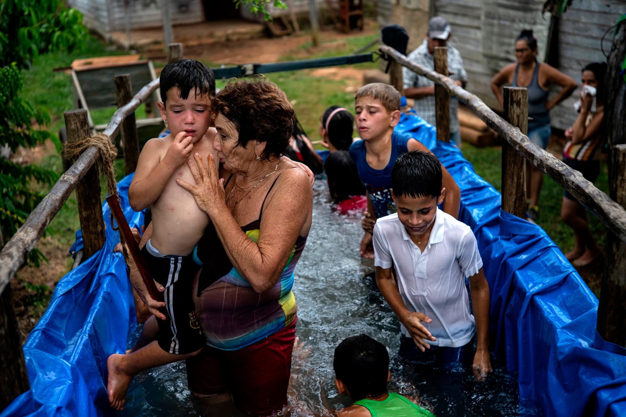En esta foto del 24 de agosto de 2019, Margarita Jiménez sostiene a un niño dentro de una piscina creada a partir de un remolque de tractor en el barrio El Infernal en San Andrés, en la provincia de Pinar del Río, Cuba. Jiménez supervisa a los niños en la piscina y les enseña a algunos a nadar. 