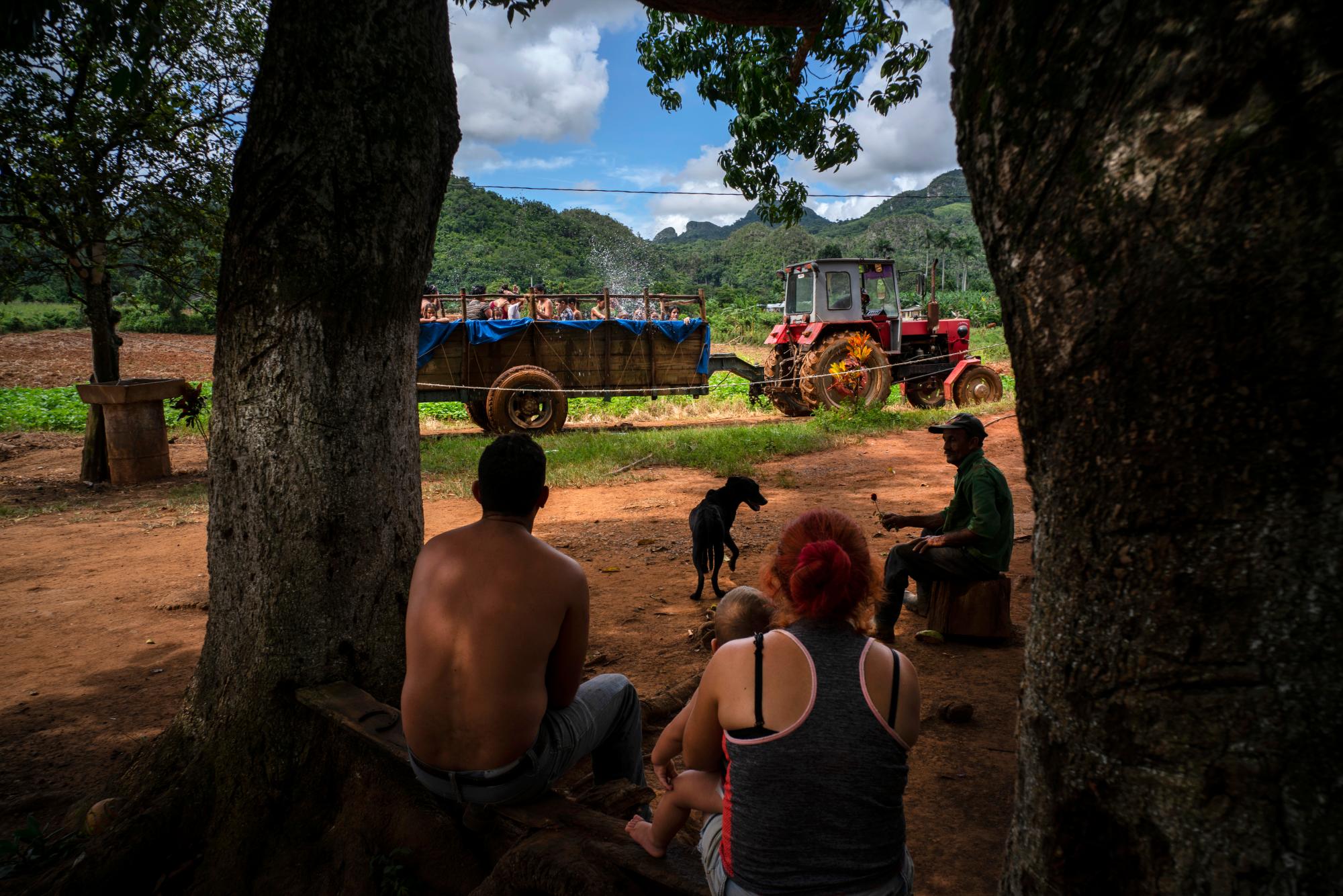 En esta fotografía del 24 de agosto de 2019, una familia sentada en la sombra observa un tractor con una piscina rodante en el vecindario de El Infernal, en la provincia de Pinar del Río, Cuba. 