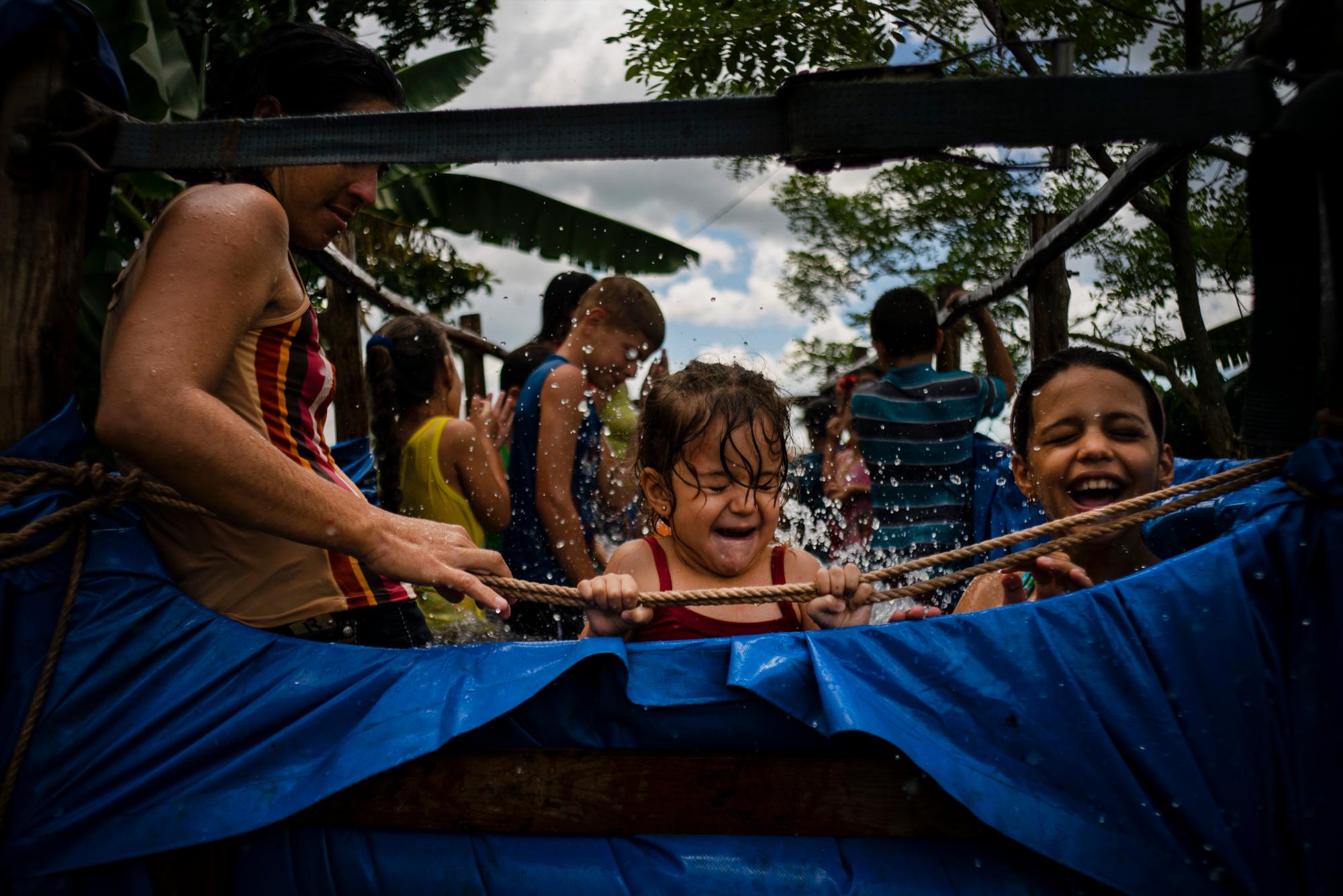 En esta fotografía del 24 de agosto de 2019, una niña se sostiene de la cuerda de una piscina móvil creada en el remolque de un tractor en el vecindario de El Infernal, en la provincia de Pinar del Río, Cuba. 