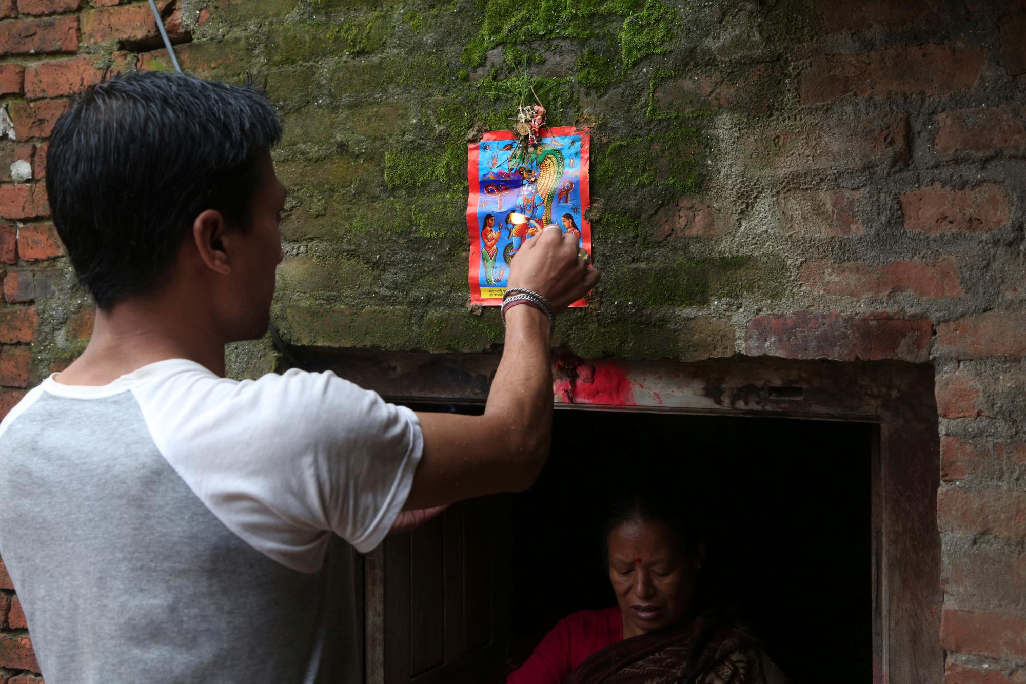 En esta foto del 5 de agosto de 2019, un hombre nepalí sujeta una lámina impresa a máquina sobre la puerta de su casa durante el festival de Naag Panchami en Bhaktapur, Nepal.