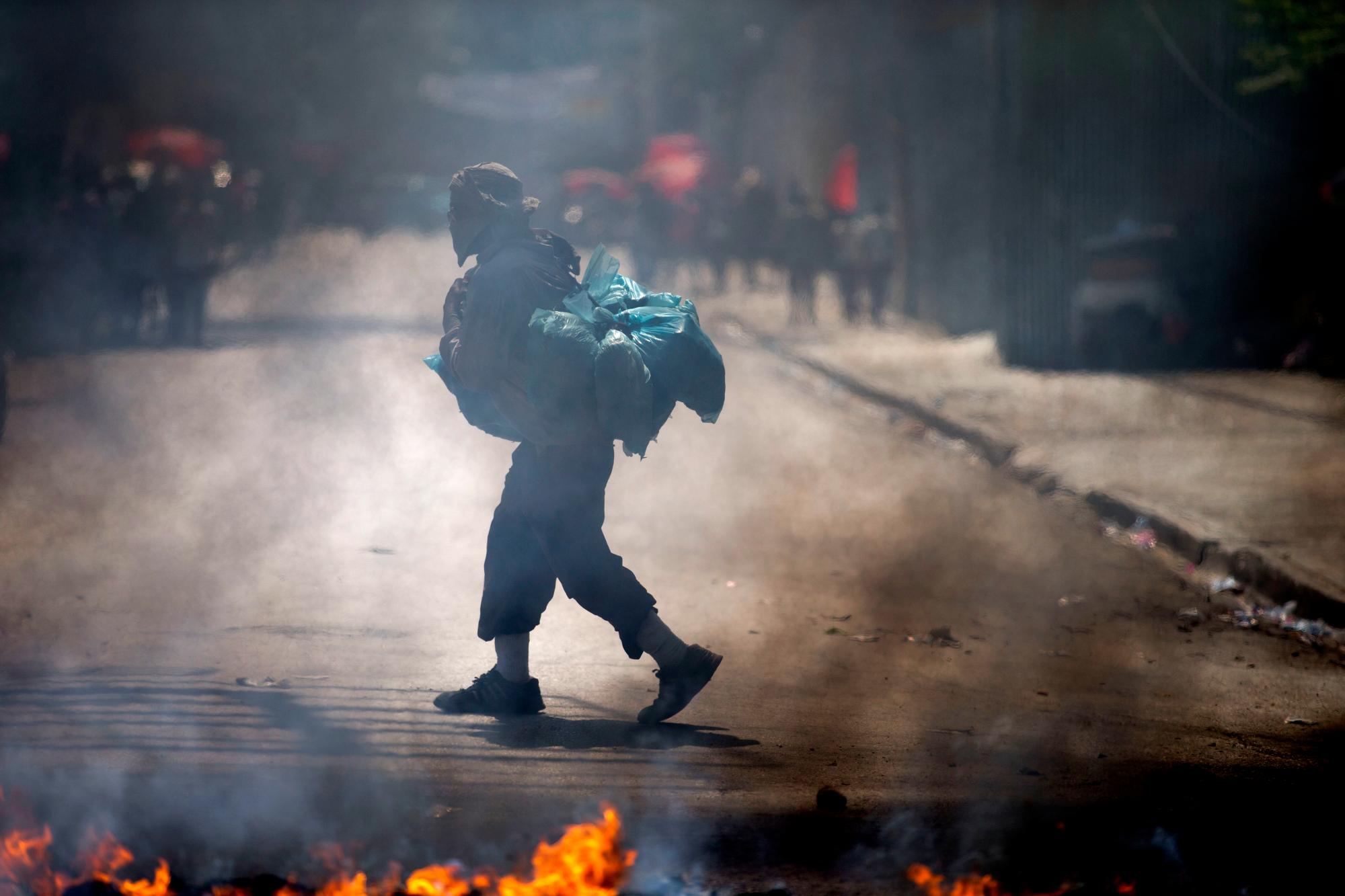 Un hombre pasa frente a un obstáculo en llamas establecido por personas que protestaban por la escasez de combustible en Puerto Príncipe, Haití, el lunes 2 de septiembre de 2019. Las estaciones de servicio han estado reduciendo sus horas de operación durante las últimas dos semanas, y el domingo todas las estaciones estaban cerradas. 