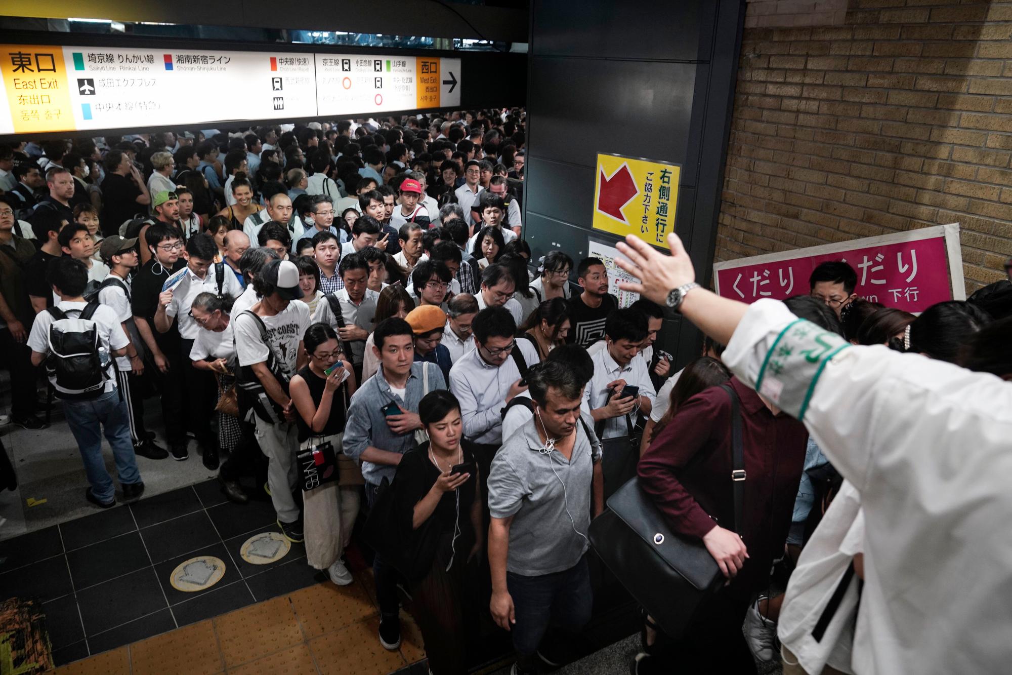 Un empleado de la estación le dice a los pasajeros que disminuyan la velocidad mientras suben las escaleras poco después de que algunas plataformas de trenes reabrieron tras retrasos el lunes 9 de septiembre de 2019 en Tokio. El tifón Faxai está soplando en el área metropolitana de Tokio, interrumpiendo los viajes, cortando el poder y causando docenas de lesiones. 