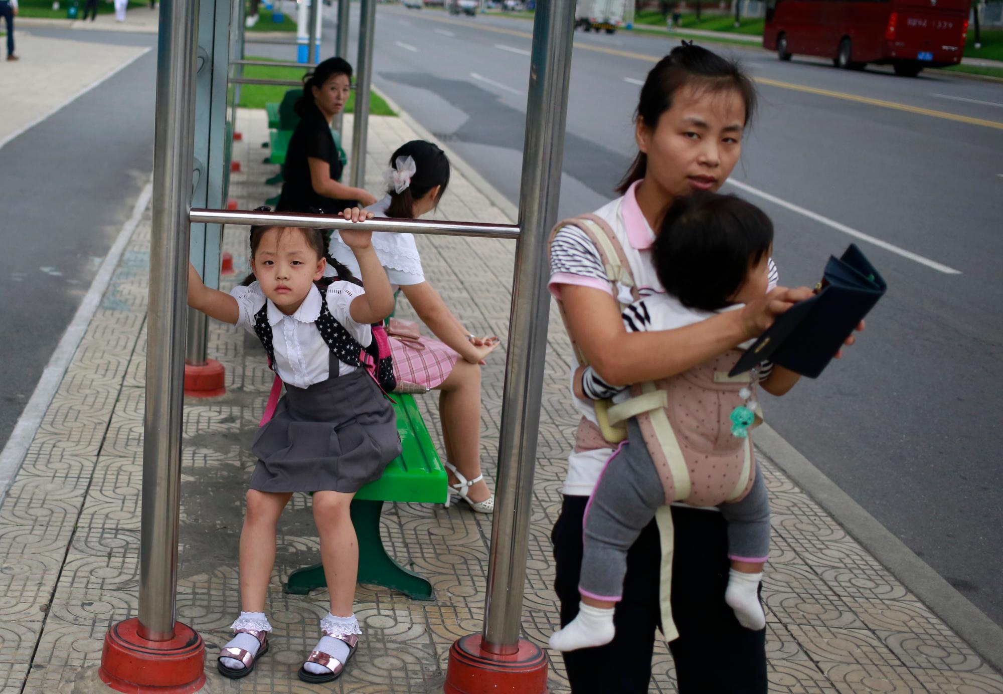 Una mujer y sus hijos esperan un autobús en una parada en la calle Mirae Scientist en Pyongyang, Corea del Norte, el jueves 12 de septiembre de 2019. 