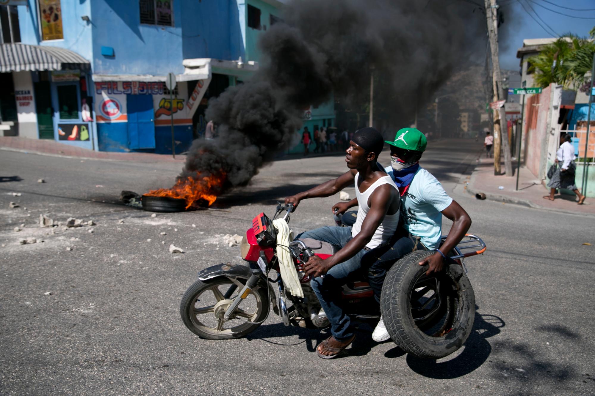 Un hombre lleva un neumático para agregar a una barricada en llamas durante una protesta contra la escasez de combustible en Petion-ville, Haití, el domingo 15 de septiembre de 2019. Las estaciones de servicio han estado reduciendo sus horas de funcionamiento en las últimas semanas y la mayoría estaban cerradas esta semana. 