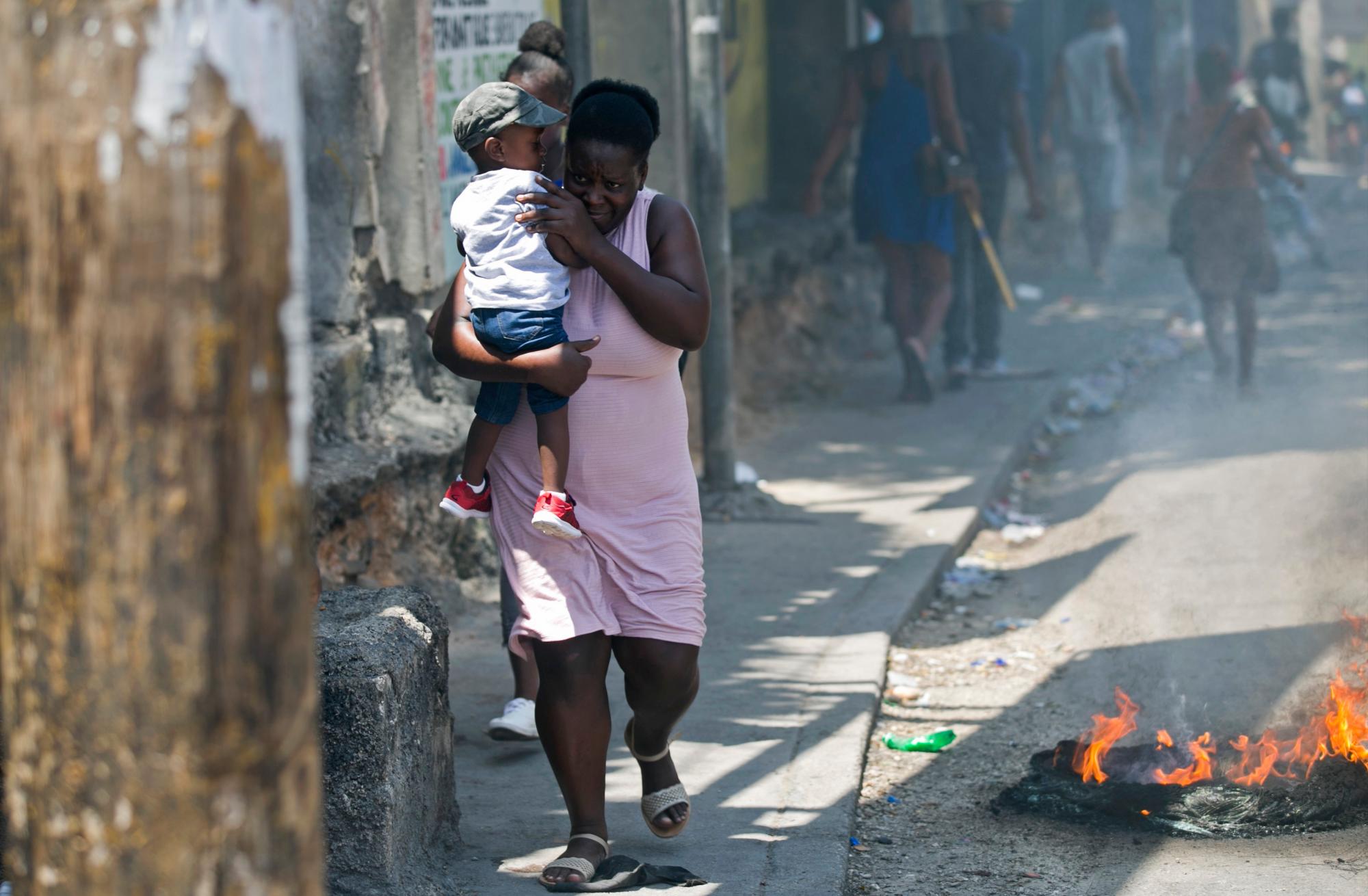 Una mujer lleva a un niño más allá de una barricada incendiada creada por personas que protestaban por la escasez de combustible en Petion-ville, Haití, el domingo 15 de septiembre de 2019. Las estaciones de servicio han estado reduciendo sus horas de funcionamiento en las últimas semanas y la mayoría cerró este semana. 