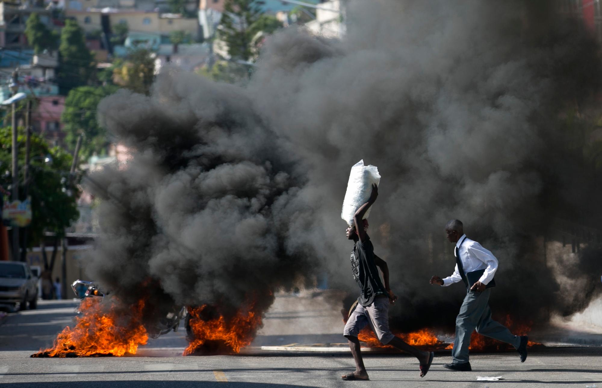La gente pasa frente a una barricada incendiada creada por personas que protestaban por la escasez de combustible en Petion-ville, Haití, el domingo 15 de septiembre de 2019. Las estaciones de servicio han estado reduciendo sus horas de operación en las últimas semanas y la mayoría cerraron esta semana. 