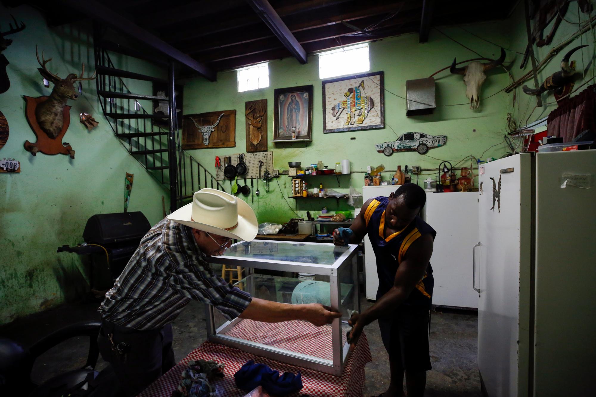 En esta foto del 30 de julio de 2019, Desidero Ojeda, a la izquierda, de Texas, trabaja con Alphat, de Uganda, en la reparación de una vitrina en la tienda de la esquina de Ojeda, cerca del refugio El Buen Pastor para migrantes, donde se hospeda Alphat, en Ciudad Juárez, México. .