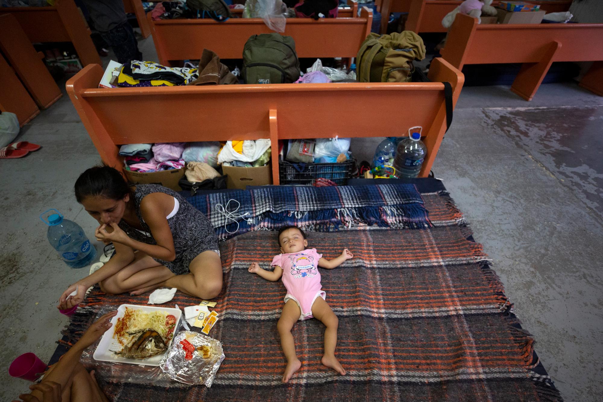 En esta foto del 28 de julio de 2019, Evelyn, de El Salvador, come un almuerzo compartido mientras su hija duerme en un área establecida para familias entre los bancos del refugio El Buen Pastor para migrantes en Cuidad Juárez, México. 