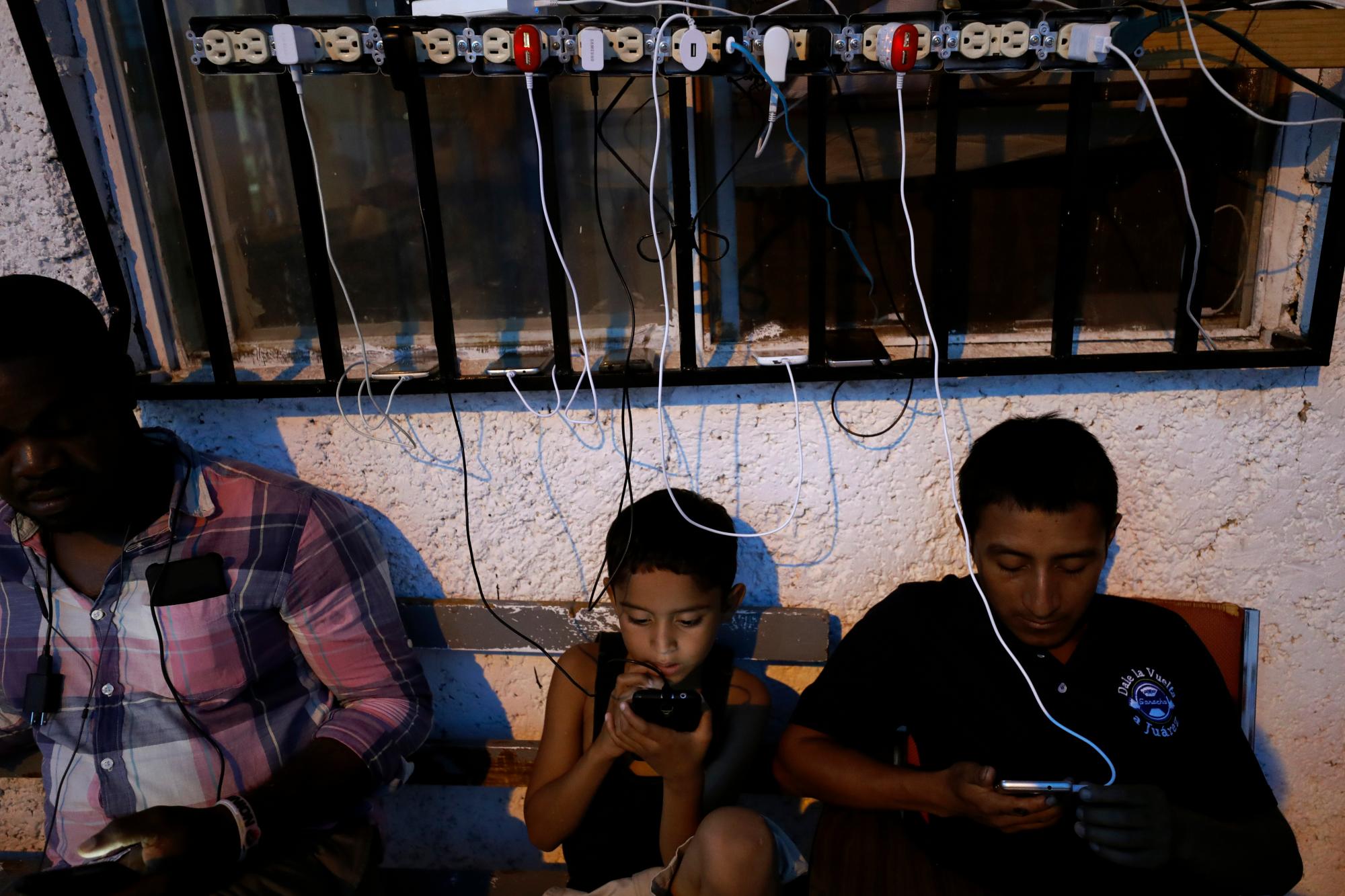 En esta foto del 30 de julio de 2019, los migrantes de África y América Latina revisan sus teléfonos entre cables de carga de teléfonos enchufados en enchufes en el refugio El Buen Pastor para migrantes en Ciudad Juárez, México. 