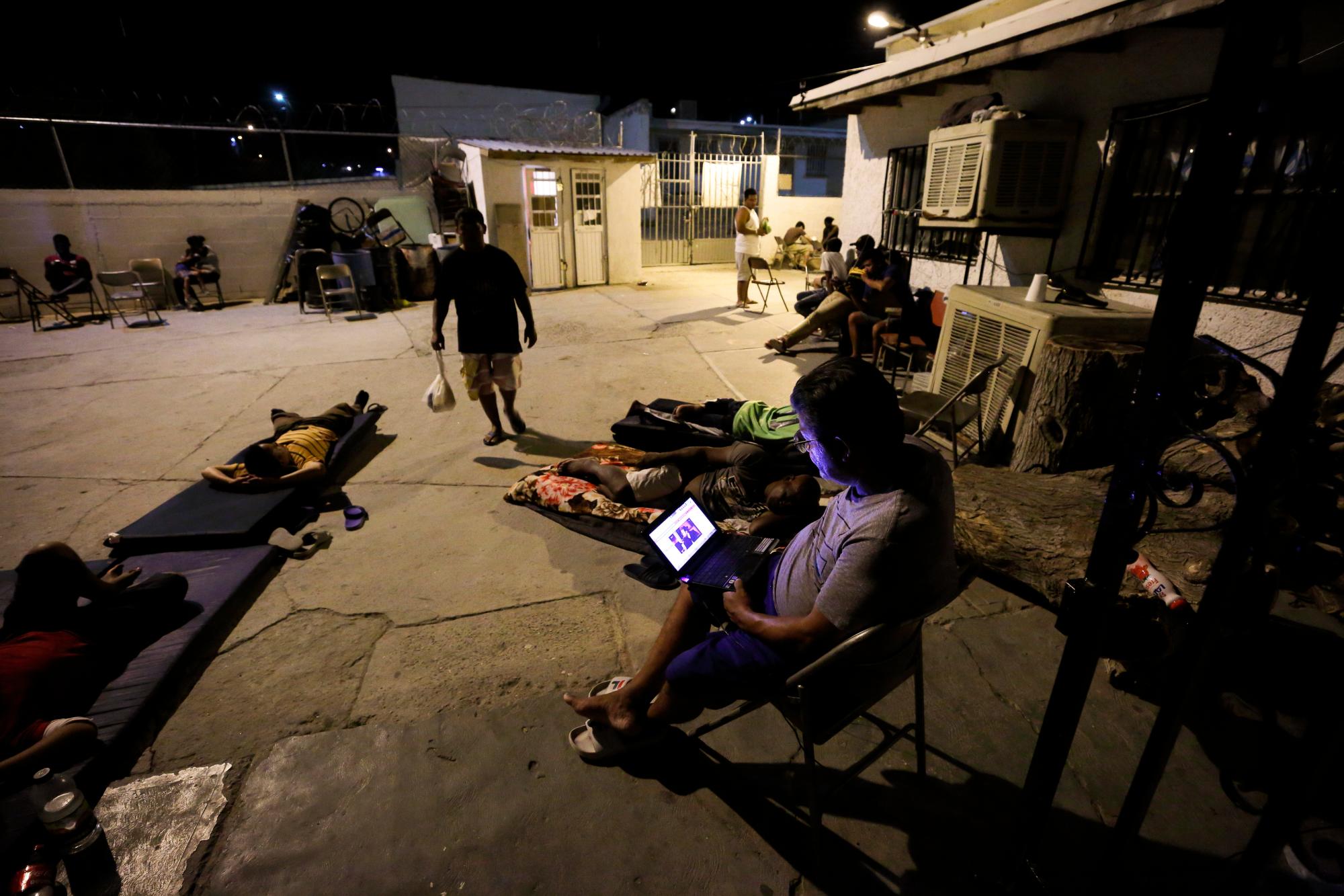 En esta foto del 25 de julio de 2019, un hombre cubano mira la pantalla de una computadora mientras otros yacen alrededor del patio en el refugio El Buen Pastor para migrantes en Ciudad Juárez, México.